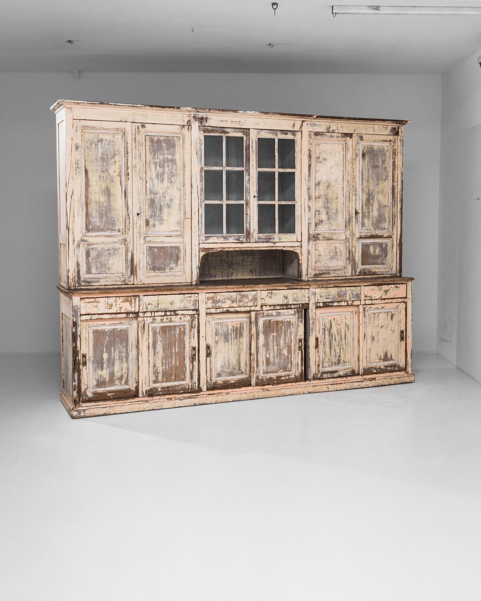 A wooden vitrine from France, produced circa 1900. A massive vitrine, standing nearly eight feet tall and stretching to a width of ten feet, this white patinated antique maintains a delicate grace: a double door display cabinet over an arched cubby
