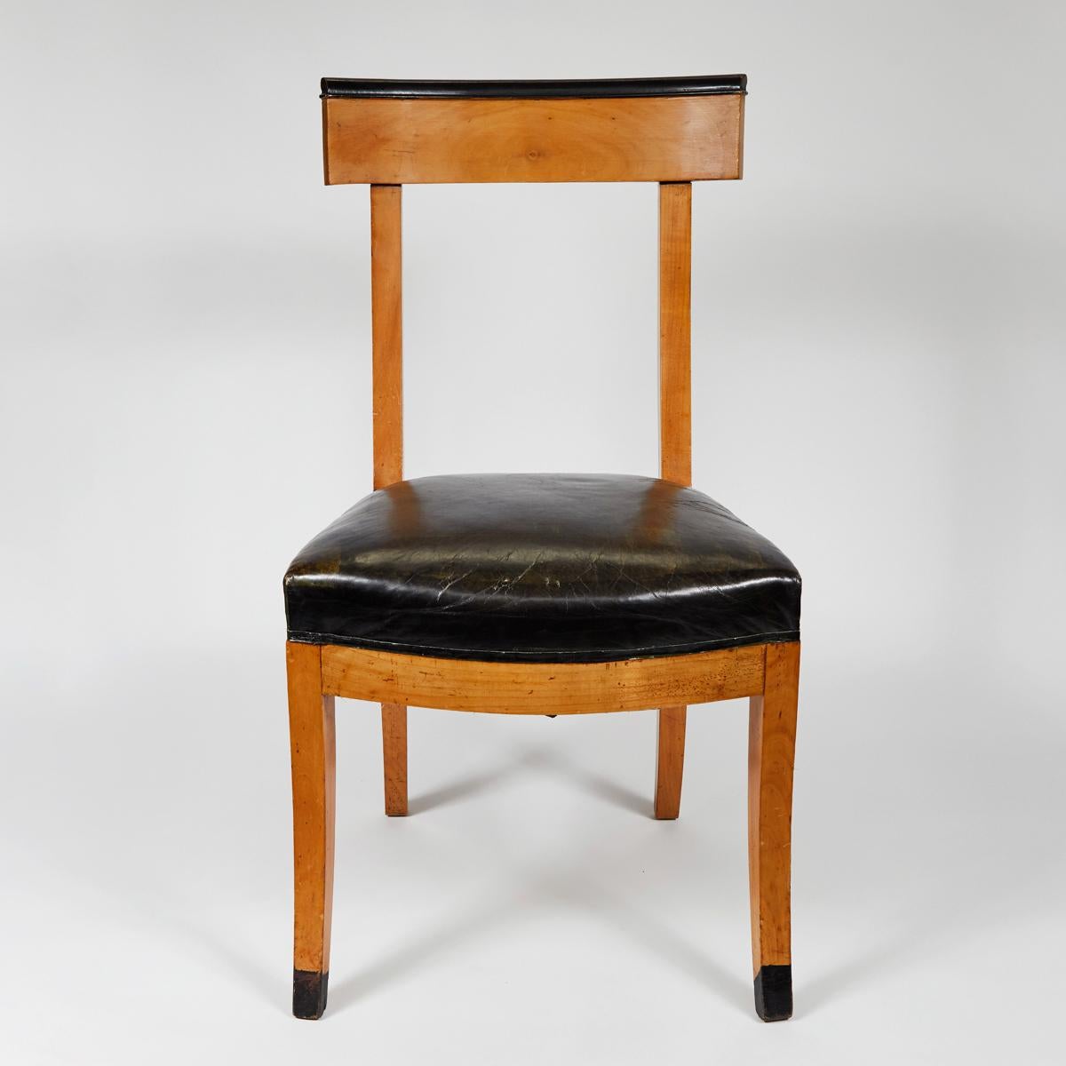 1900s French dining chairs with upholstered black leather seats. The elegant chairs are accented with ebonized back crest rails and black leather seats on saber legs.