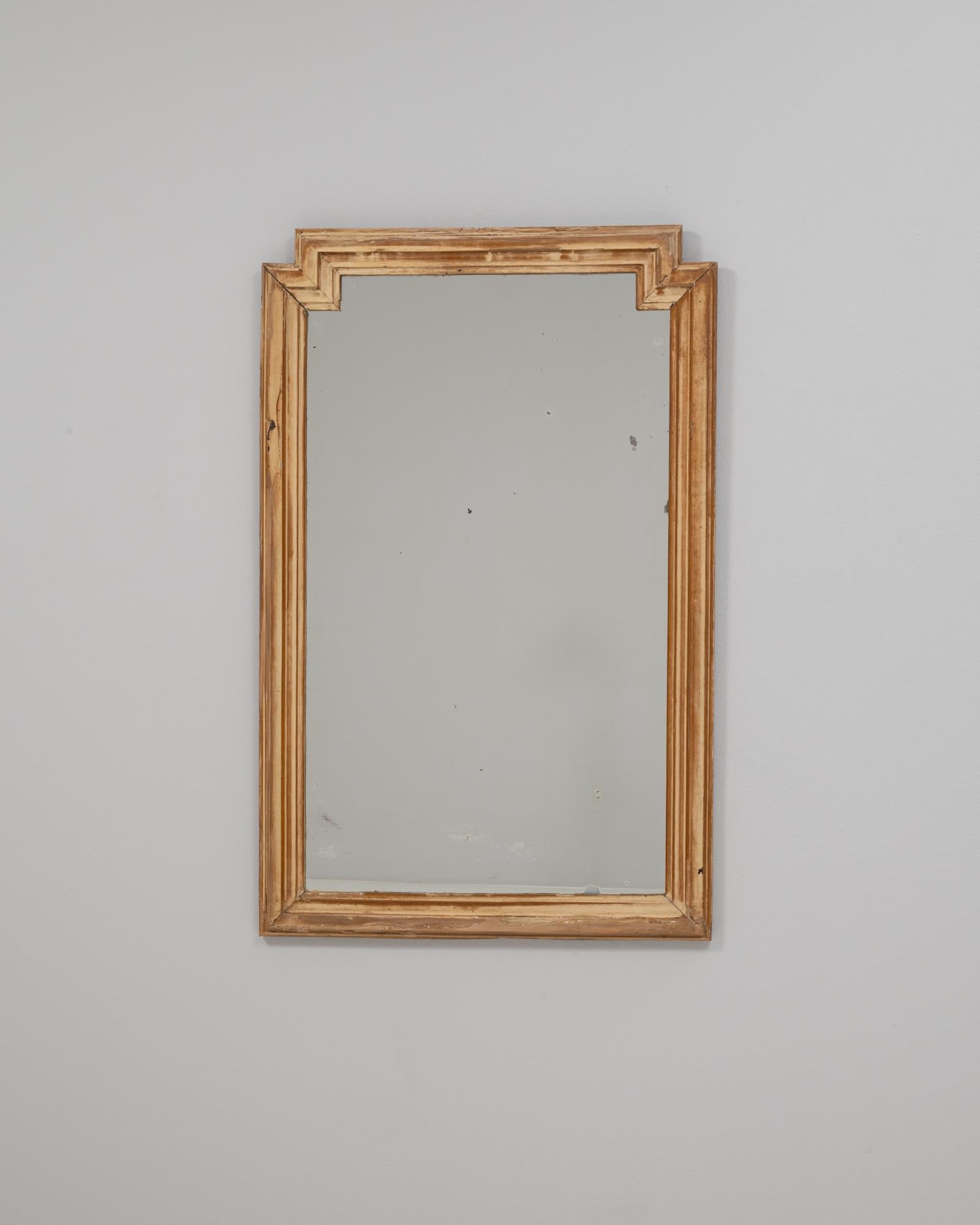 This 1900s French geometric stepped-frame wooden wall mirror offers a clean, architectural silhouette that distinguishes it from more ornate period designs. The frame features a tiered, angular profile at the top corners, creating a subtle stepped