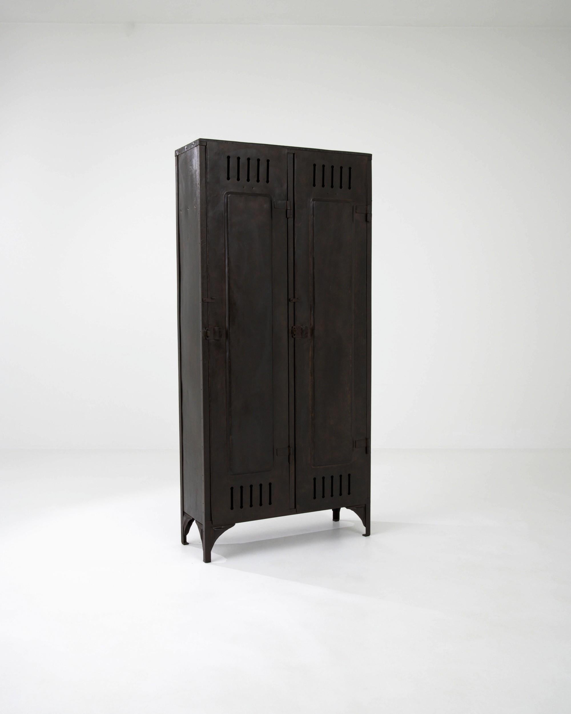 Characterized by the utilitarian aesthetic of the no-frills industrial design from the early 20th century, this 1900s French cabinet places an emphasis on practicality. It features two elongated, rectangular doors with simple locks and ventilation
