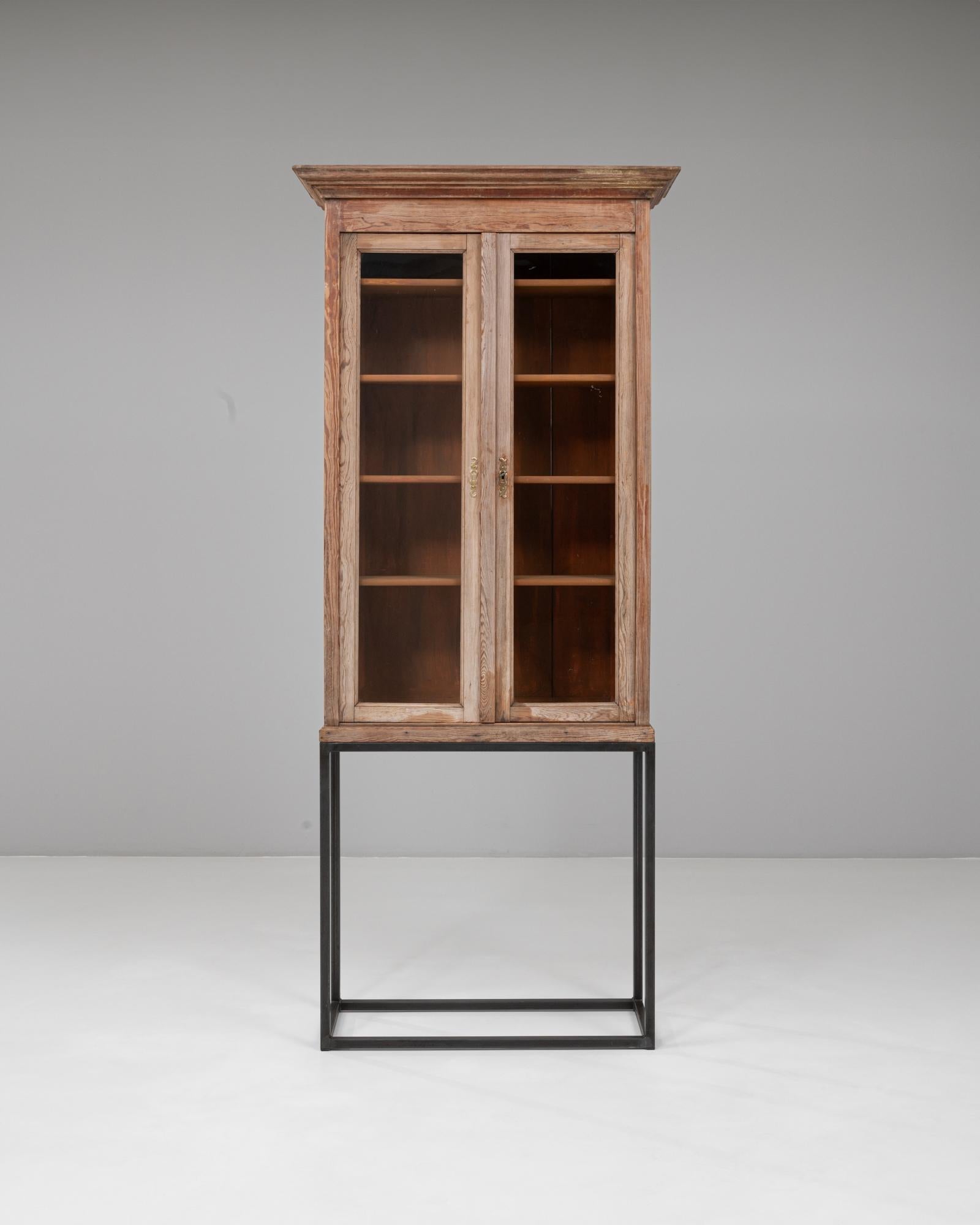 Questa vetrina industriale francese del 1900 combina un artigianato rustico con un raffinato tocco utilitaristico. Il mobile presenta la sua struttura originale in legno patinato con ante rivestite in vetro che si aprono per rivelare diversi ripiani