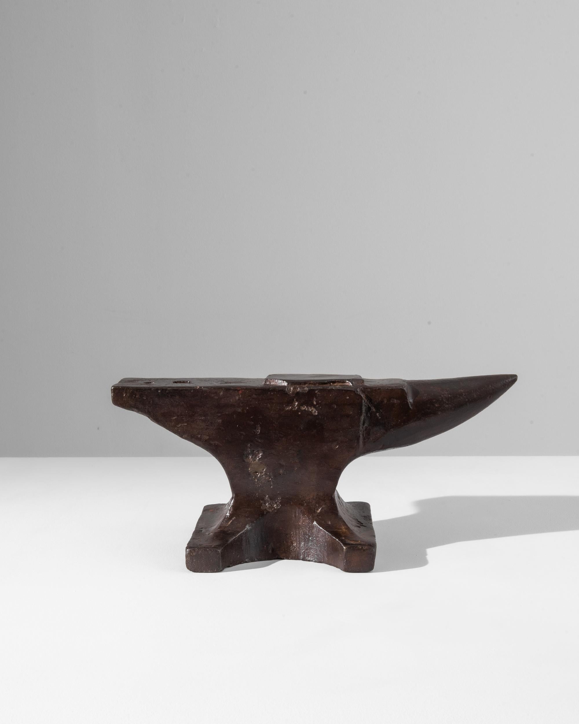 A turn of the century iron anvil produced in France, this peculiar antique exhibits the sheen of an age-old patina. Polished by beaten metal and industrious hands, the iron displays an intense brown tone with a ruby gleam, contrasted by