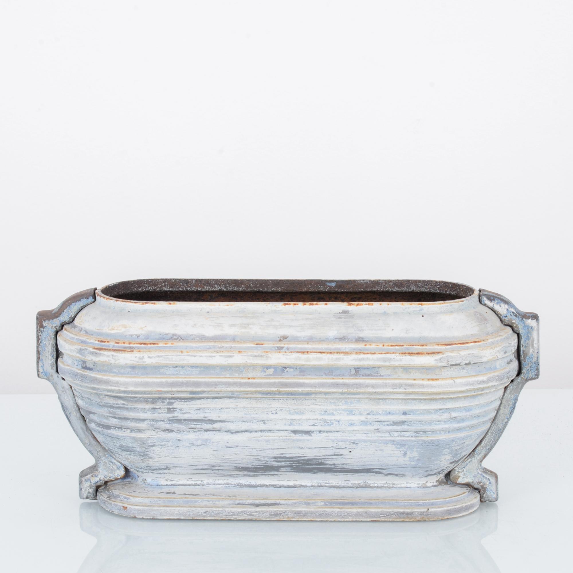 This cast iron planter was made in France, circa 1900. The horizontal details around the body sets off its unique stadium-shaped design. It stands on a stepped base and features holders on the sides. The bluish-white patina imparts a rustic quality