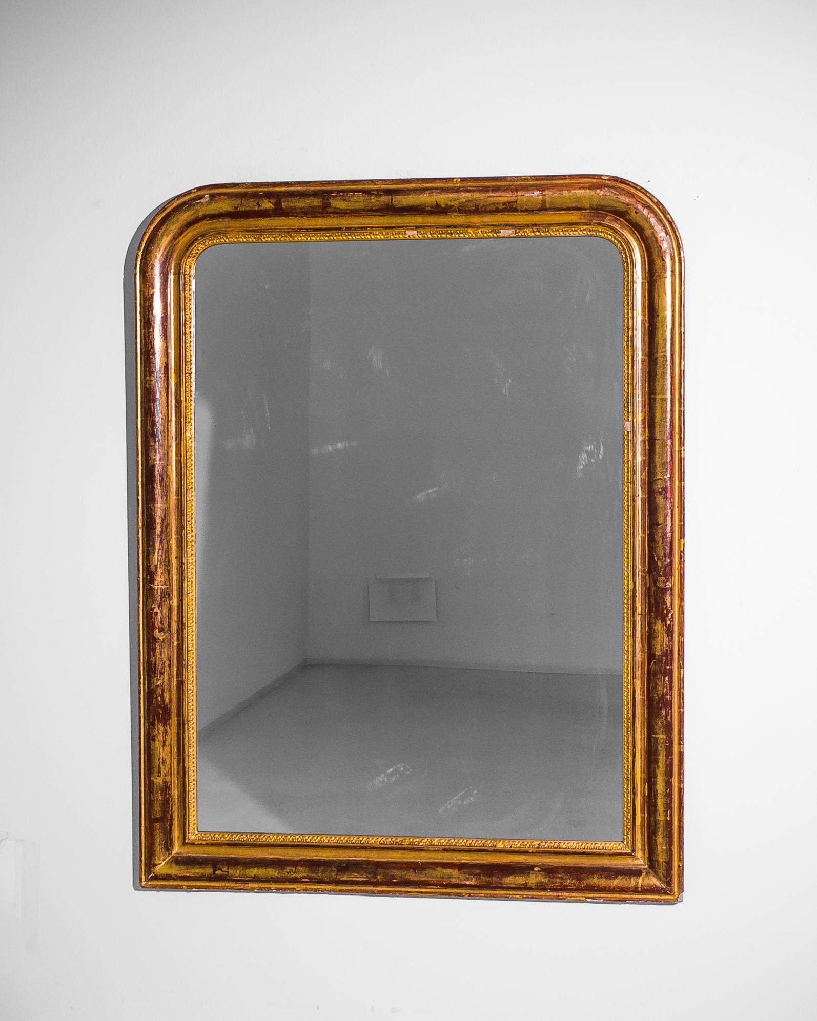 Made in 1900 in France, this antique Louis Philippe mirror presents a characteristic outline shaped by rounded top corners, squared off at the bottom. The inner border of the frame flaunts meticulous carvings accentuated by a gilded finish, the red