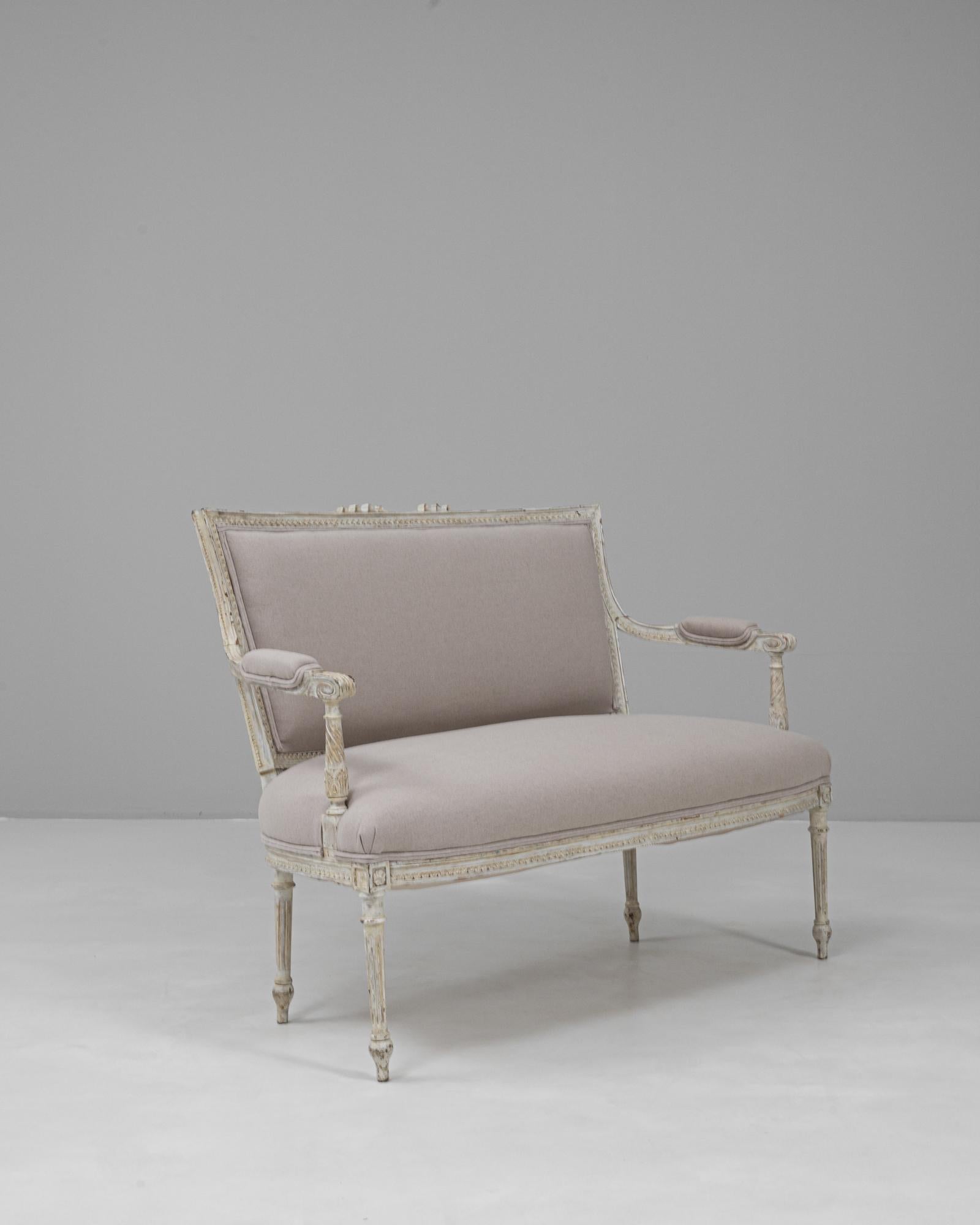 Ce canapé Louis XVI français des années 1900 présente l'élégance raffinée caractéristique de l'ère néoclassique. Le cadre en bois sculpté conserve des traces de sa finition peinte d'origine, mettant en valeur les motifs floraux complexes, les pieds