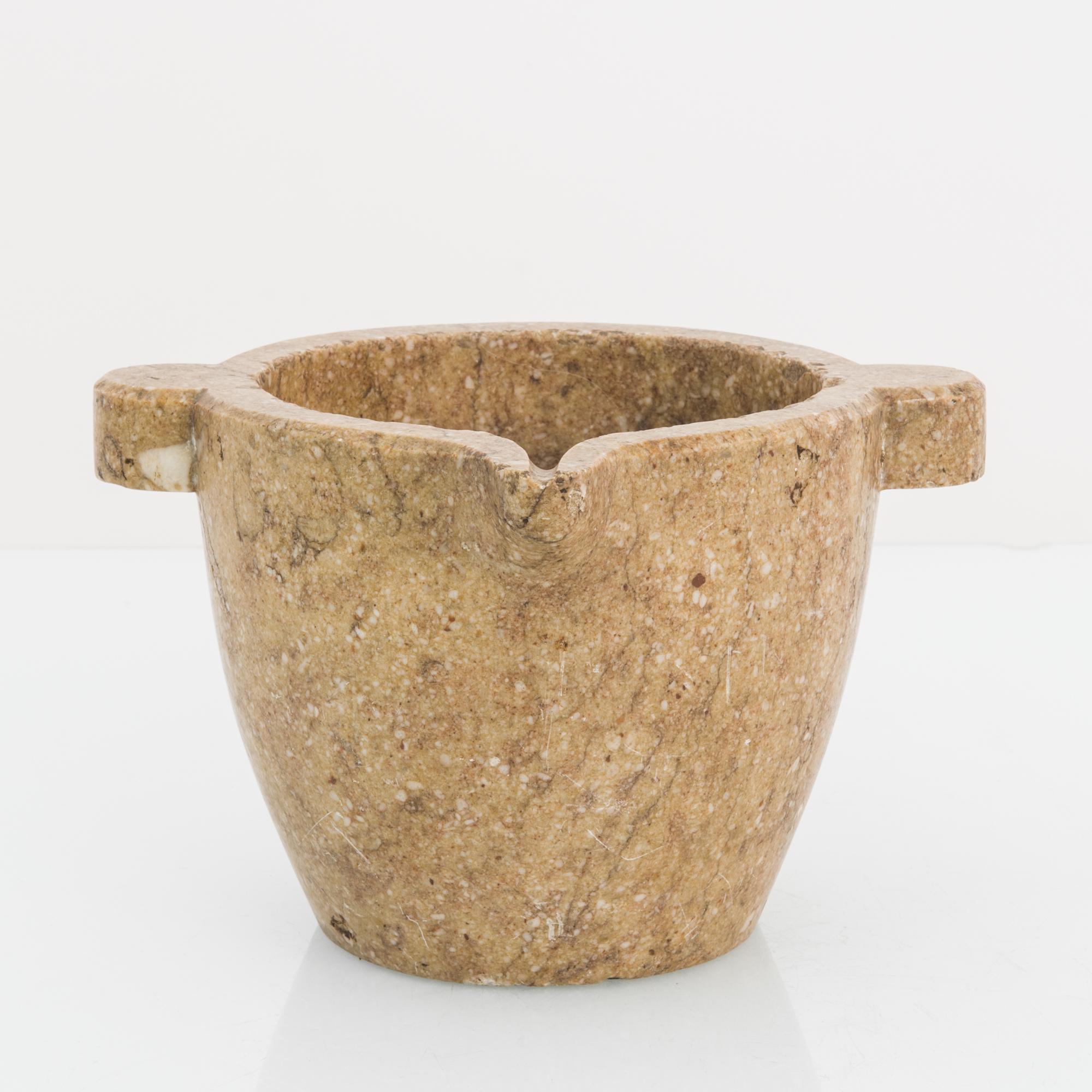 A stone mortar from France, circa 1800. Rustic and refined, the mortar is shaped from a single piece of caramel beige marble; the textural quality of the stone gifts it an immediate tactile appeal. Two stout handles around the rim lend a cardinal