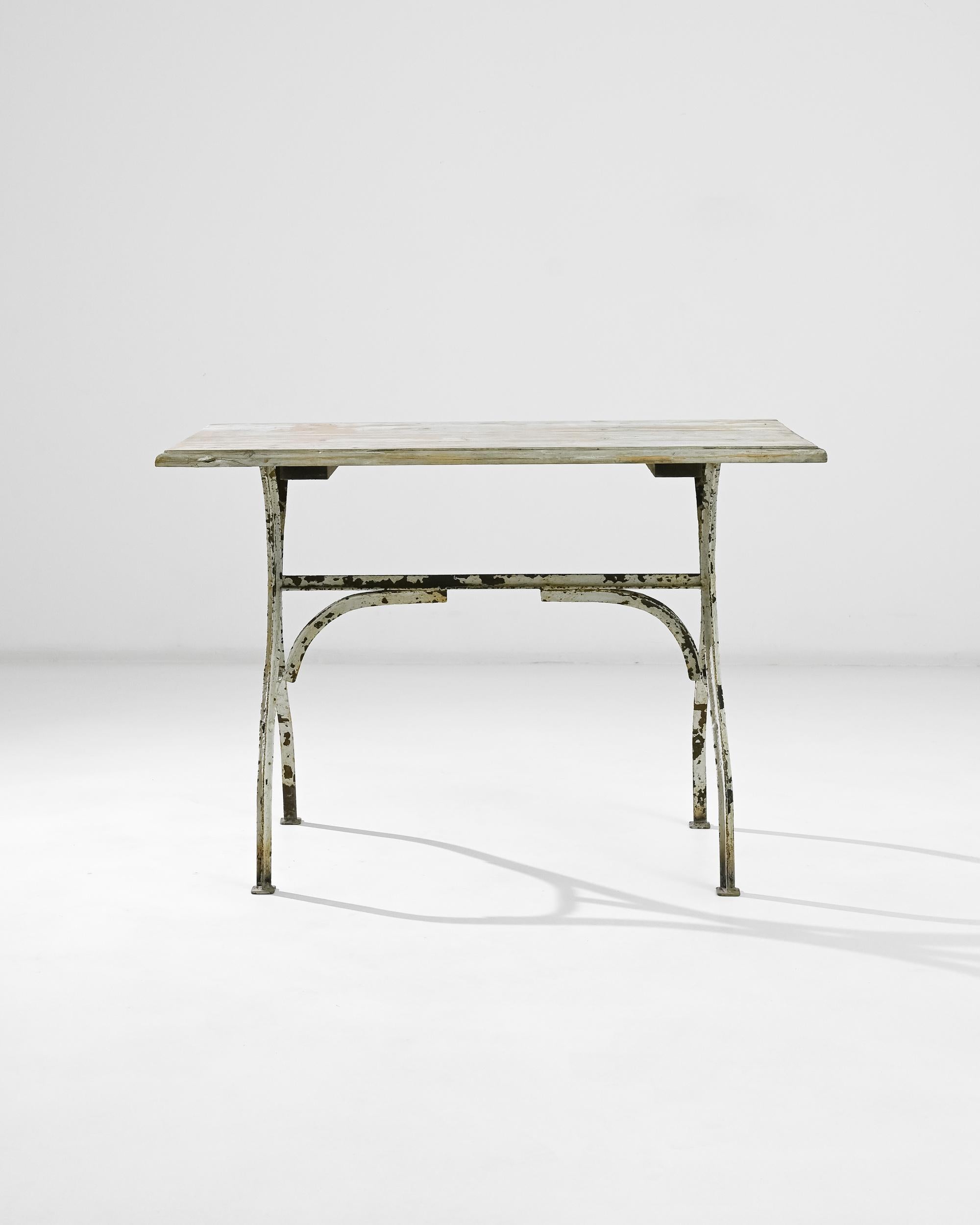 This metal and wooden table was made in France circa 1900. The rectangular tabletop is raised on a riveted metal base, the simple design is held together with a trestle, its supportive armature evoking architectural forms. The characteristic