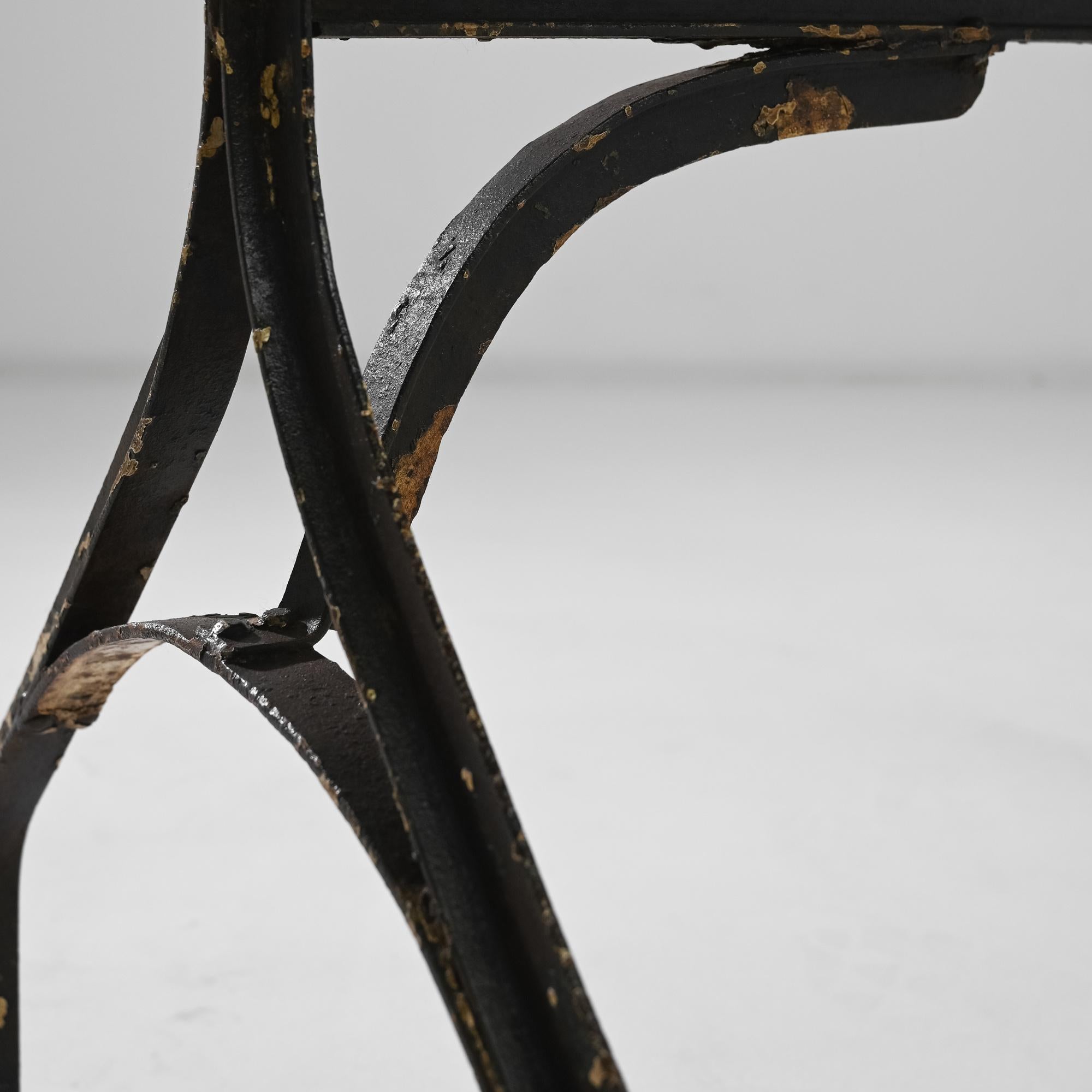 This metal and wooden table was made in France circa 1900. The rectangular tabletop is raised on a riveted metal base, the simple design is held together with a trestle, its supportive armature evoking architectural forms. The characteristic