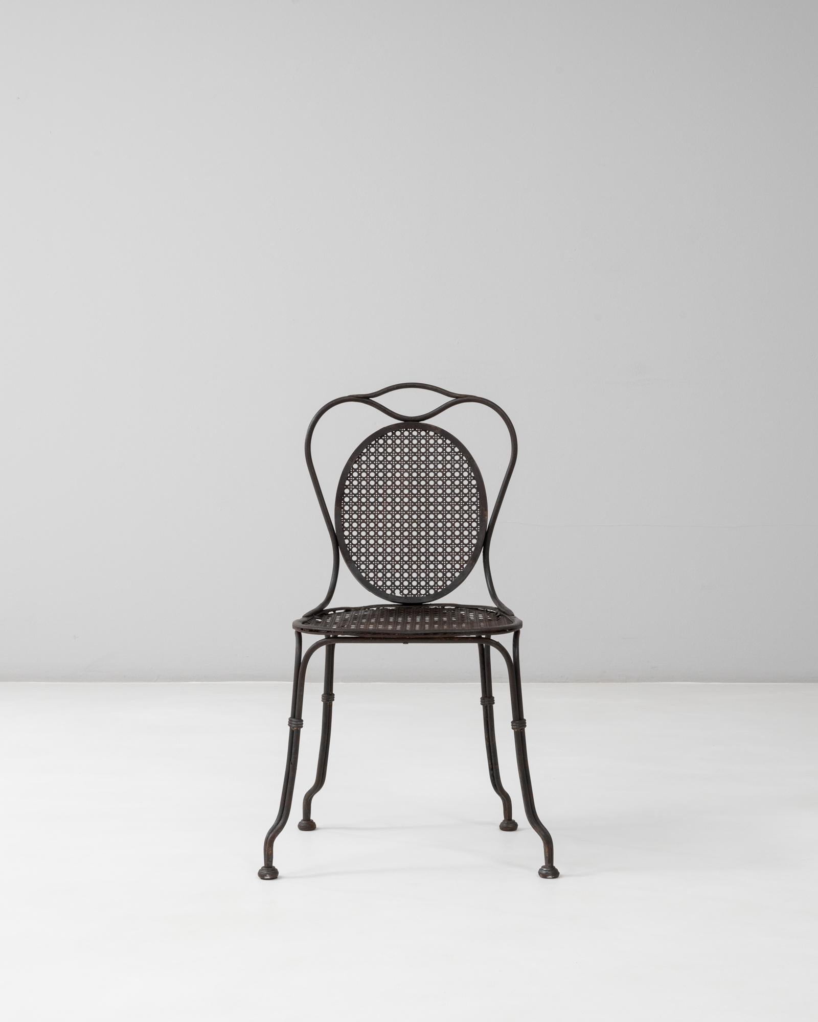 Questa sedia da giardino francese del 1900 in metallo con schienale ovale mostra i graziosi dettagli artigianali caratteristici dei primi arredi da bistrot e da giardino. La sua struttura elegantemente sagomata è formata da sottili aste di metallo,
