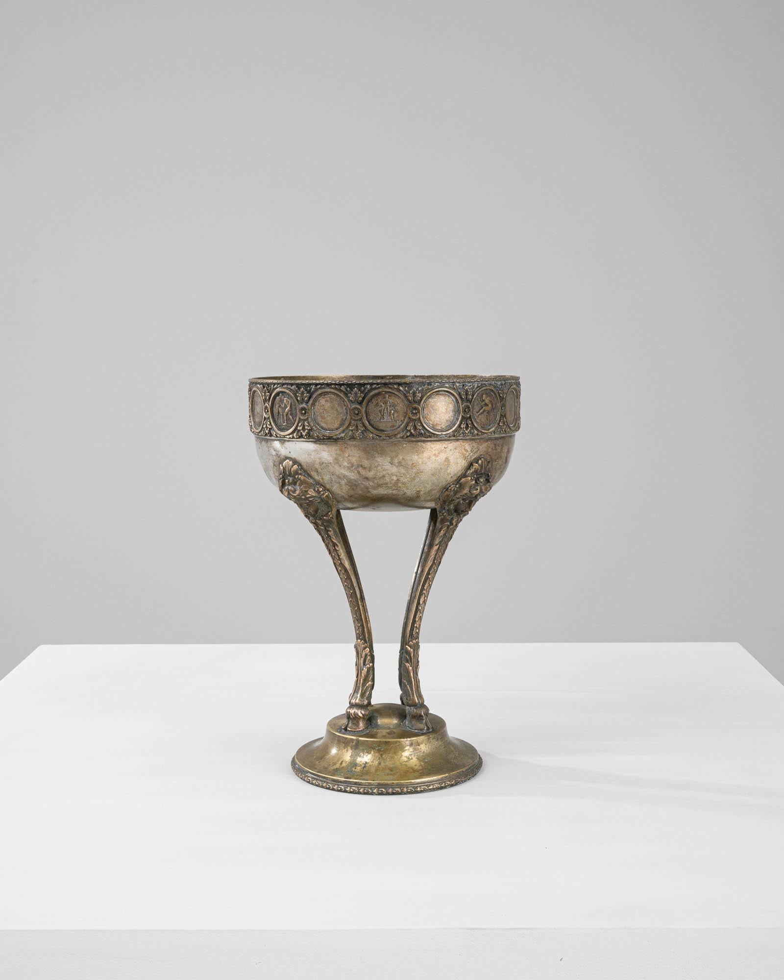 This 1900s French Metal Goblet is a true embodiment of eclectic elegance, marrying the refined Art Nouveau style with a touch of whimsy. Atop its solid circular base rise four slender hooves, a nod to neoclassical motifs, which hold the chalice