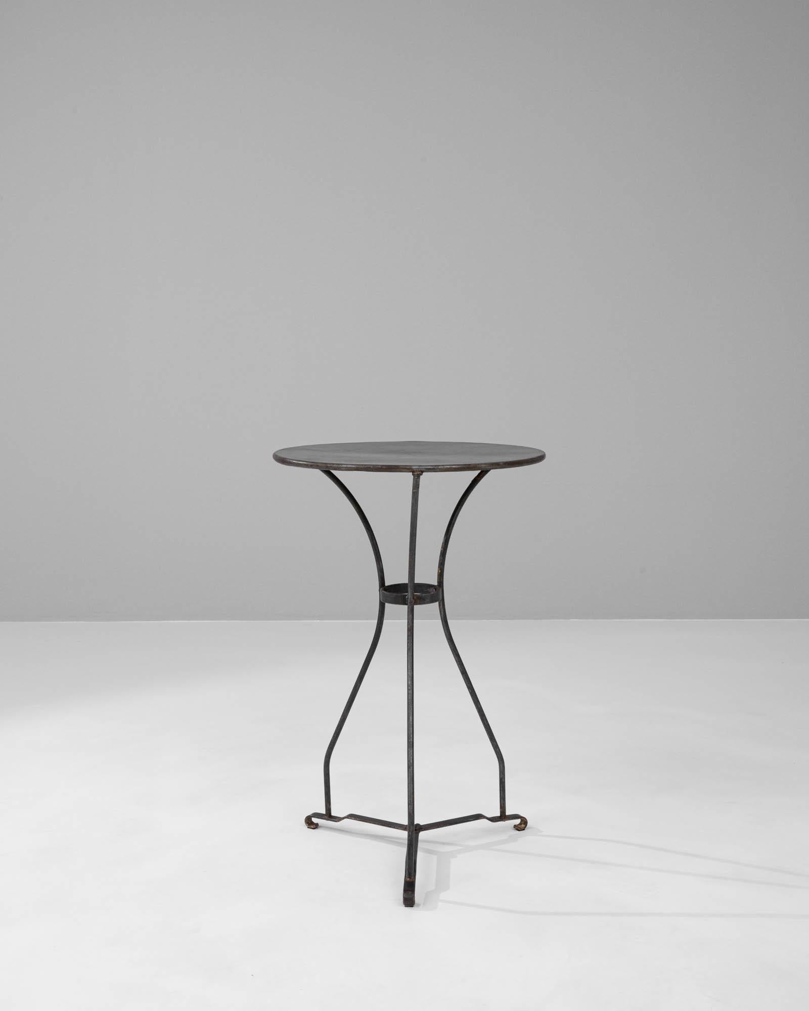 This early 1900s French metal side table is a charming artifact that carries the essence of Parisian chic and the solidity of industrial craftsmanship. Its slender, curved legs gently splay outwards, meeting the ground with delicate yet sturdy feet,