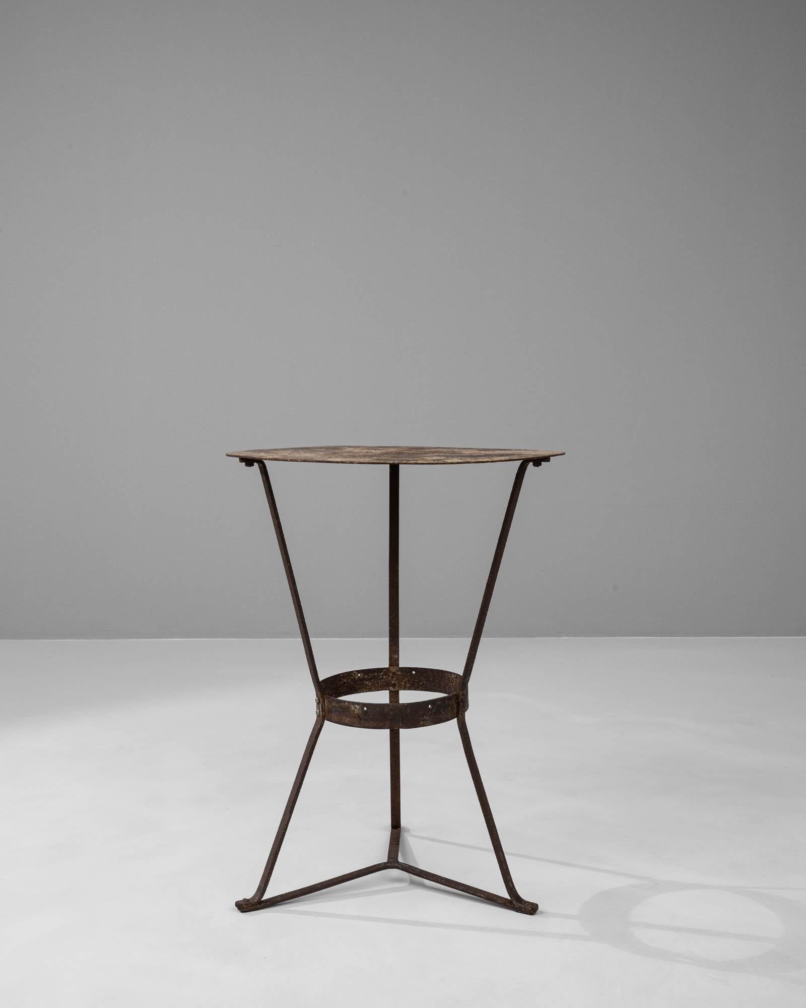 This early 1900s French metal side table embodies the industrial elegance of the era, presenting a simple yet impactful design. The clean lines of its triangular base form a delicate but stable structure, culminating in a circular top that is modest