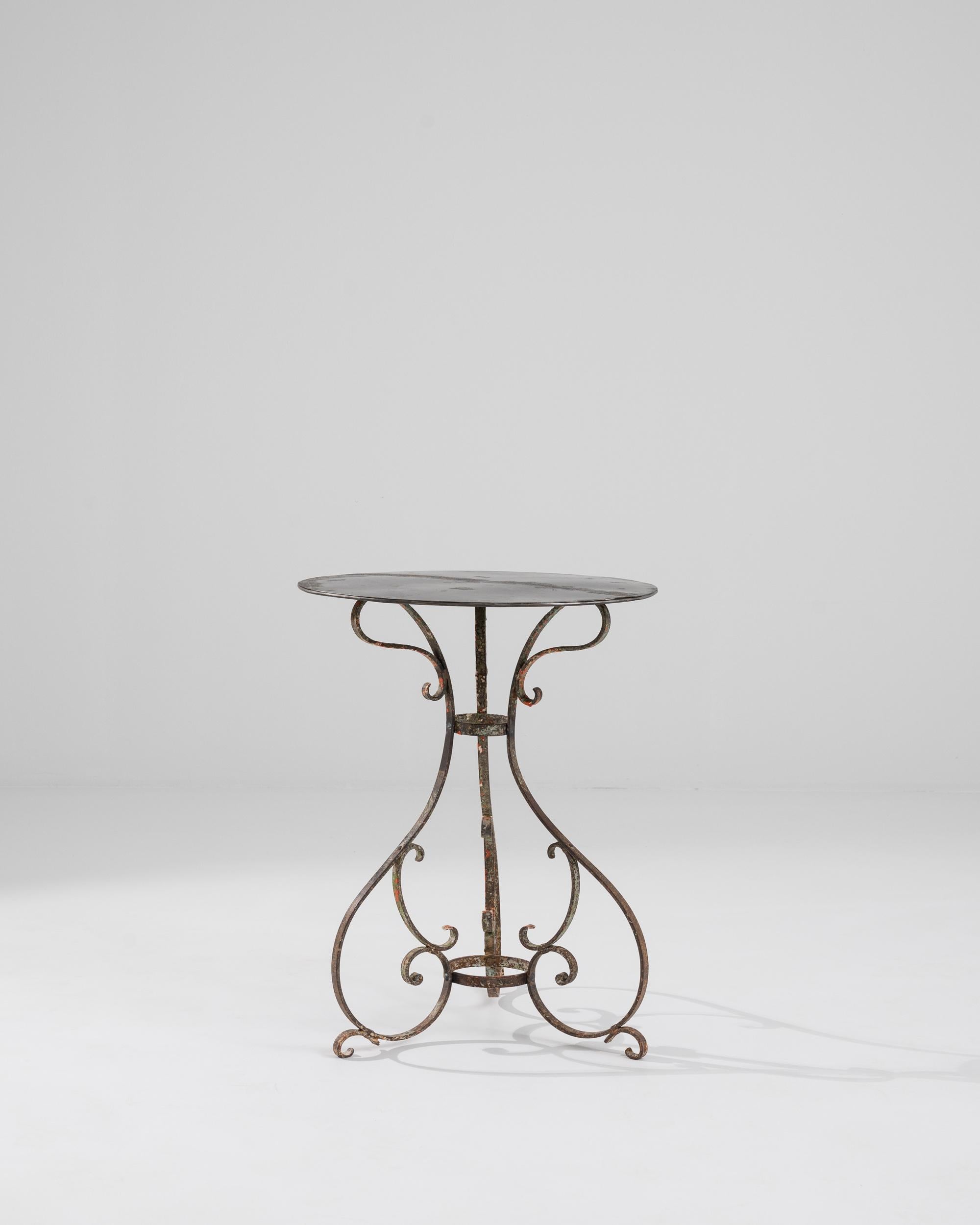 A metal table made in 1900s France. Three metal legs spiral downwards, creating a playfully animated pattern that undergirds this pleasant garden table. Reds, greens, and browns intermingle to form a curious patina, which is spread across its