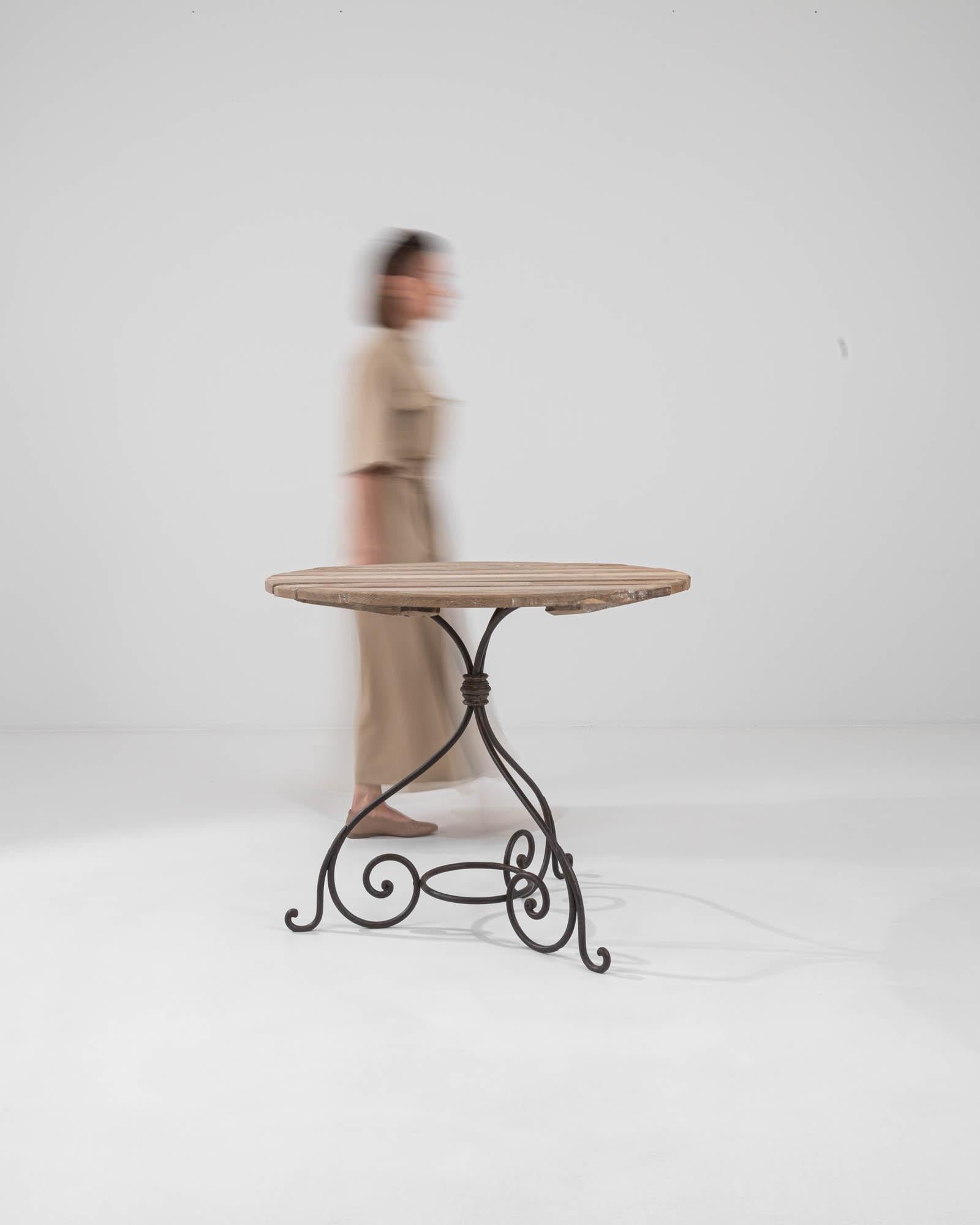 Discover the perfect blend of rustic charm and industrial flair with this 1900s French Metal Table, boasting a genuine wooden top. The circular tabletop, with its warm wood tones and visible grain, sits atop an elegantly crafted metal base whose
