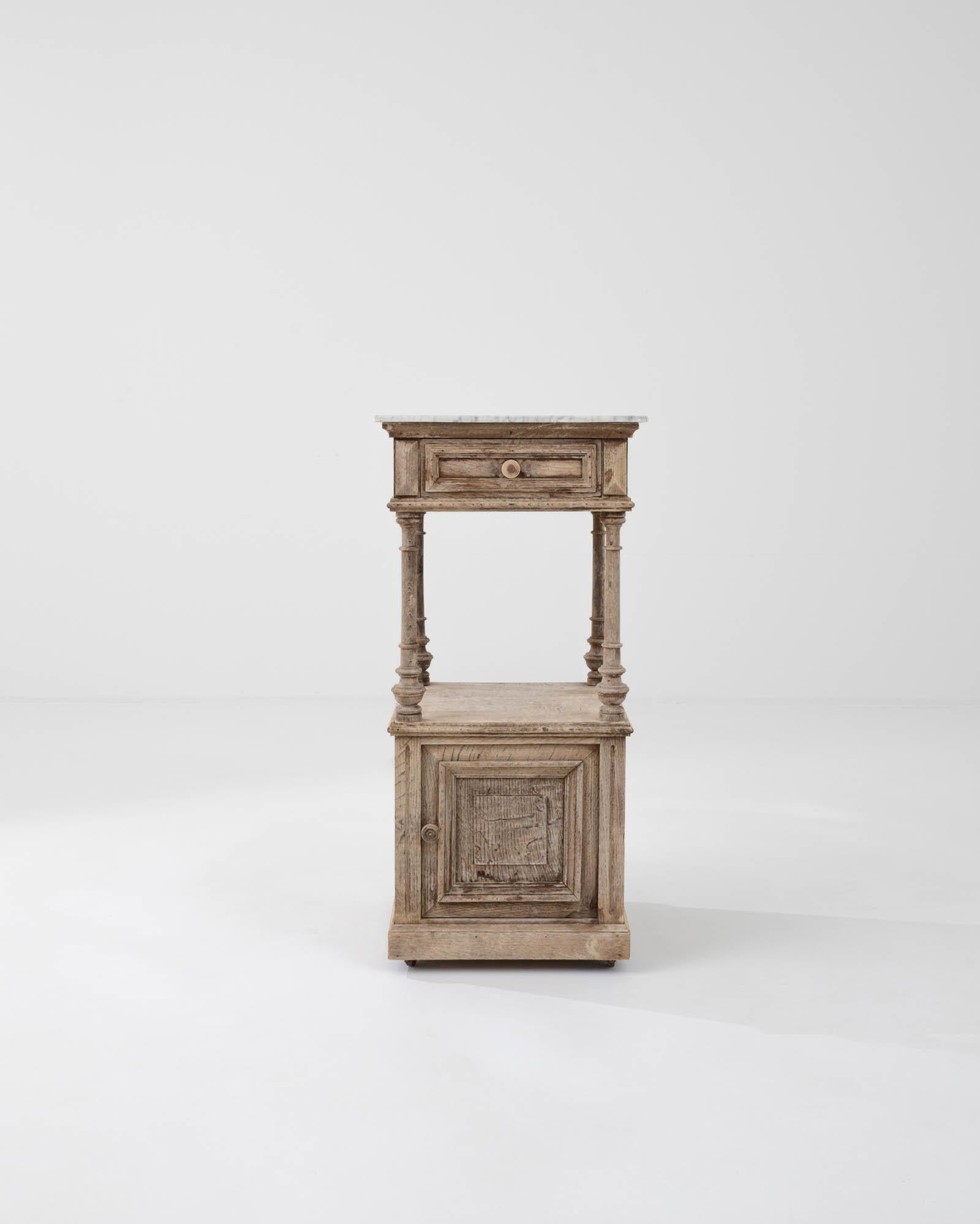 An oak night stand on wheels created in France circa 1900. Traditionally crafted, this subtly styled bedside table is adorned with a marble top, projecting a sense of calm and refined elegance. Cloudy gray veins drift through the ivory colored