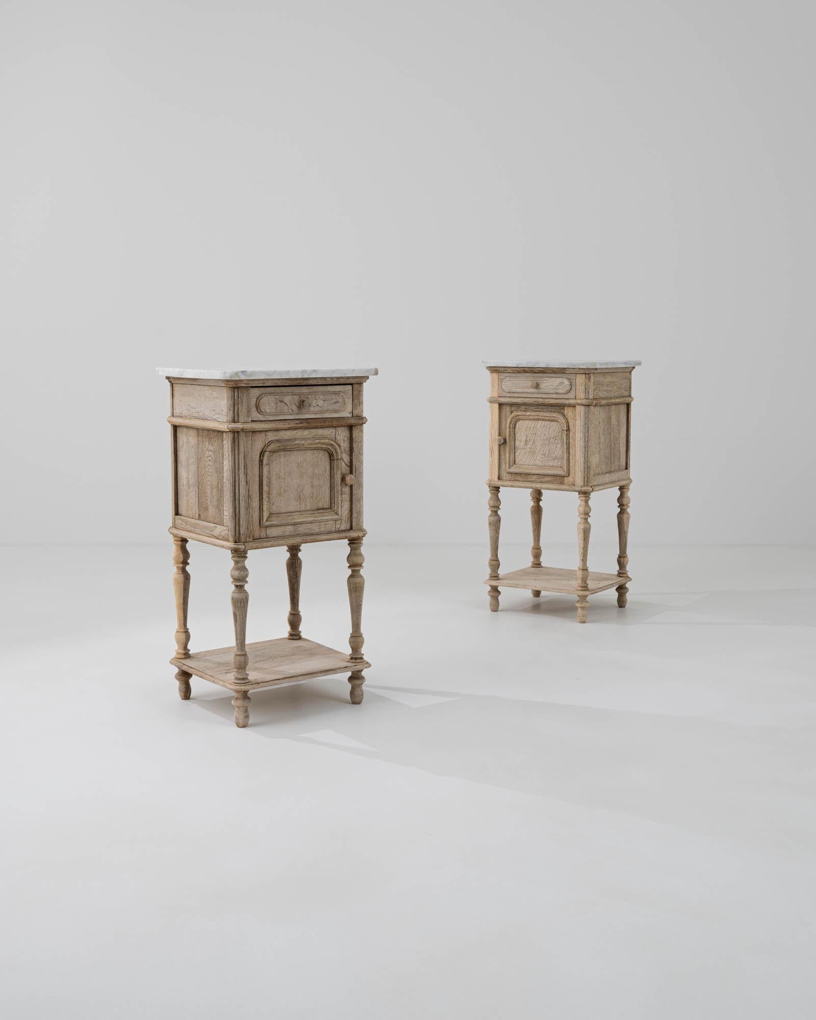 A pair of oak night stands created in France circa 1900. Traditionally crafted, this subtly styled bedside table is adorned with a marble top, projecting a sense of calm and refined elegance. Cloudy gray veins drift through the ivory colored marble