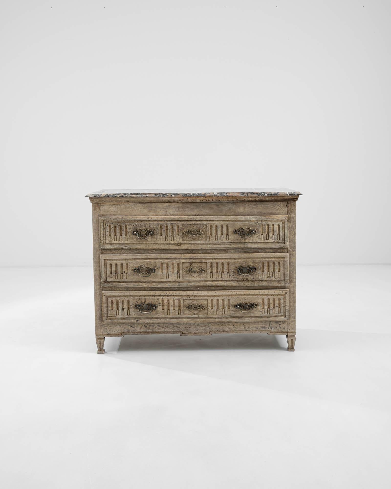 A wooden chest of drawers with a marble top created in France, circa 1900. Ornate and delicately crafted, this antique chest of drawers exudes a sense of classical elegance and studious attention to detail. Diamonds, carved into the side panels,