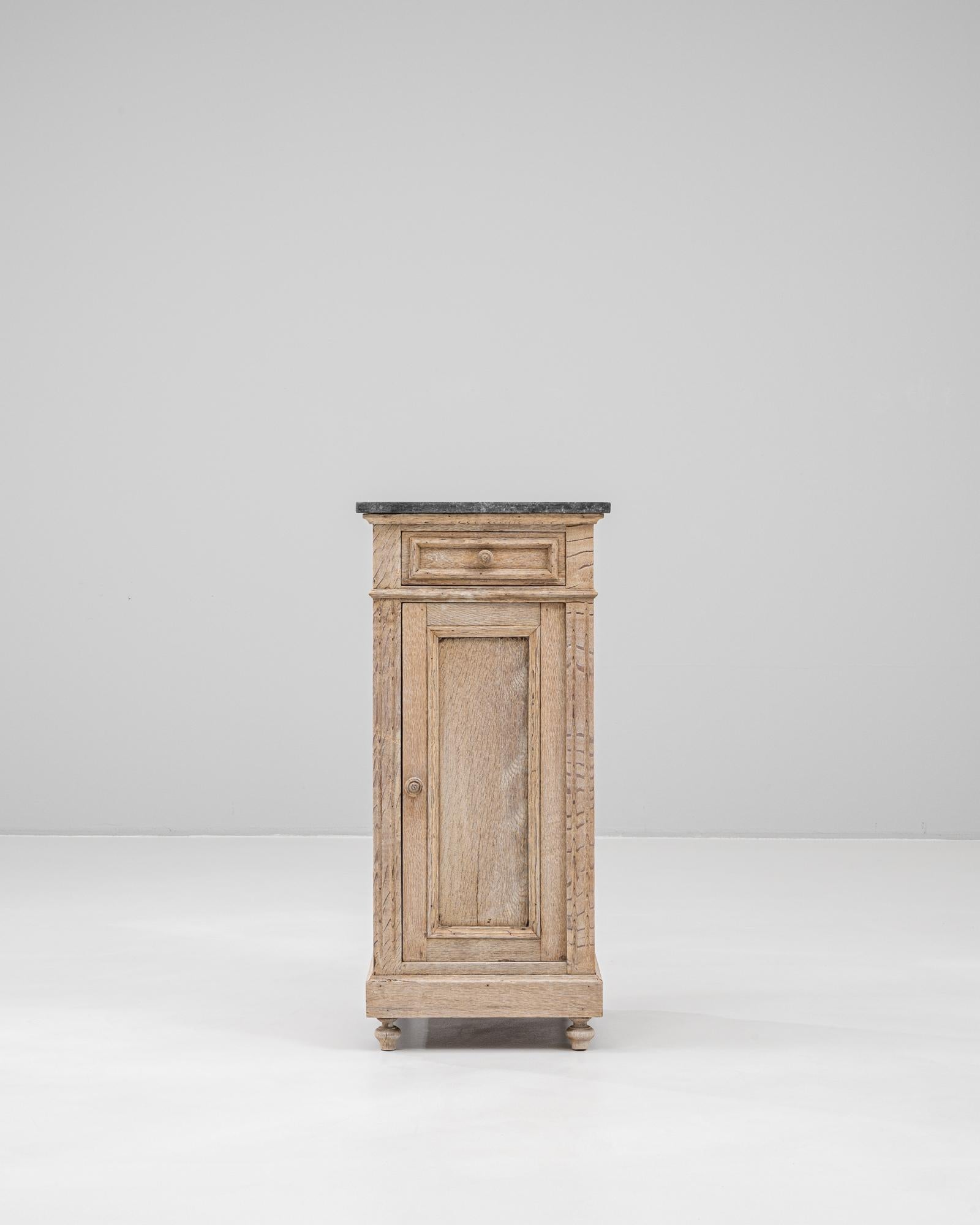 This 1900s French oak bedside table features a refined blend of natural texture and understated elegance. The light oak frame showcases subtle carved detailing along the edges, standing on petite turned feet that add a traditional touch. A single