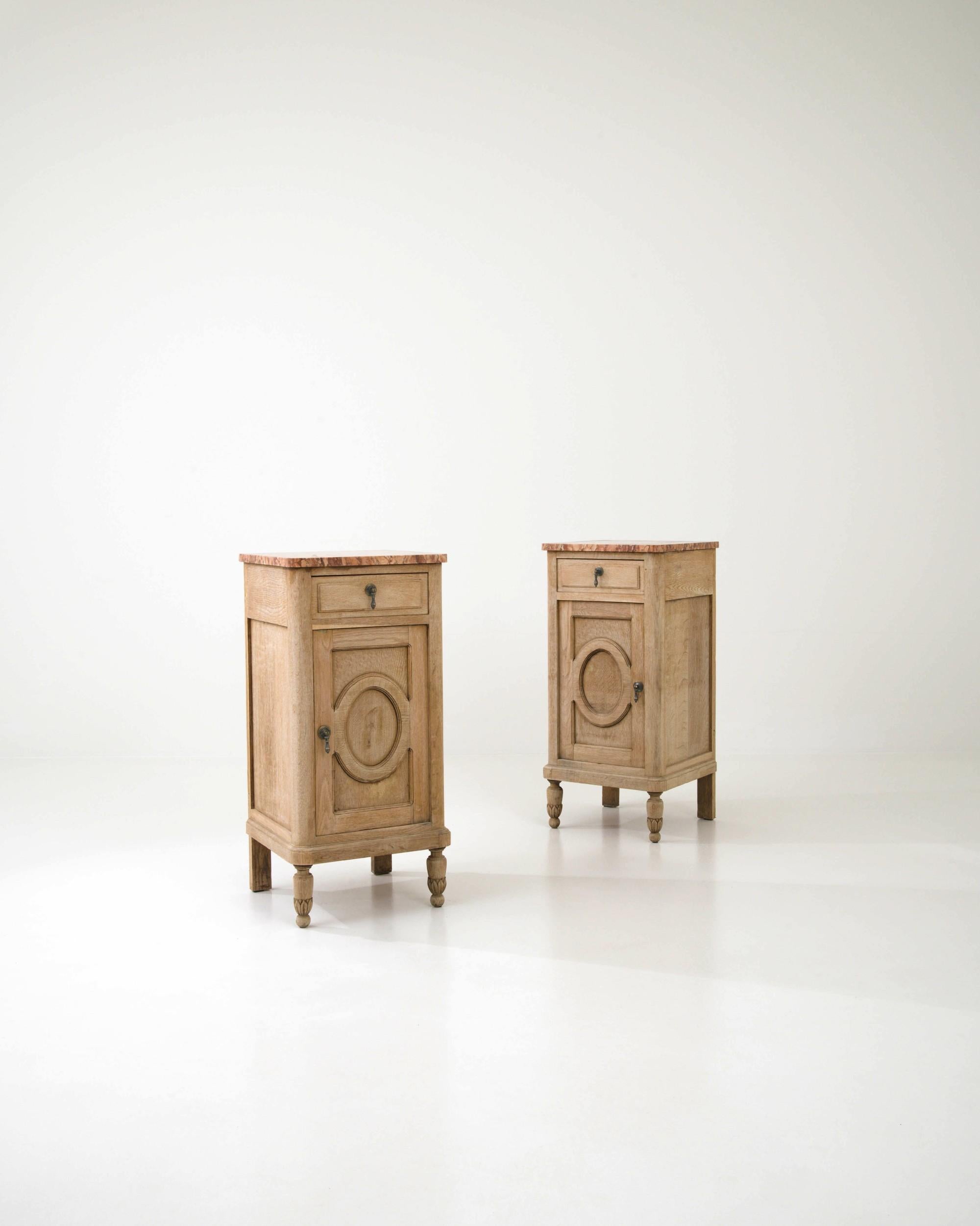 These charming nightstands were hand-crafted in 1900s France. Elevated on masterfully carved turned legs, the bedside tables feature stylish geometric detailing on the doors and exquisite pink marble tops that complement the pale finish of the