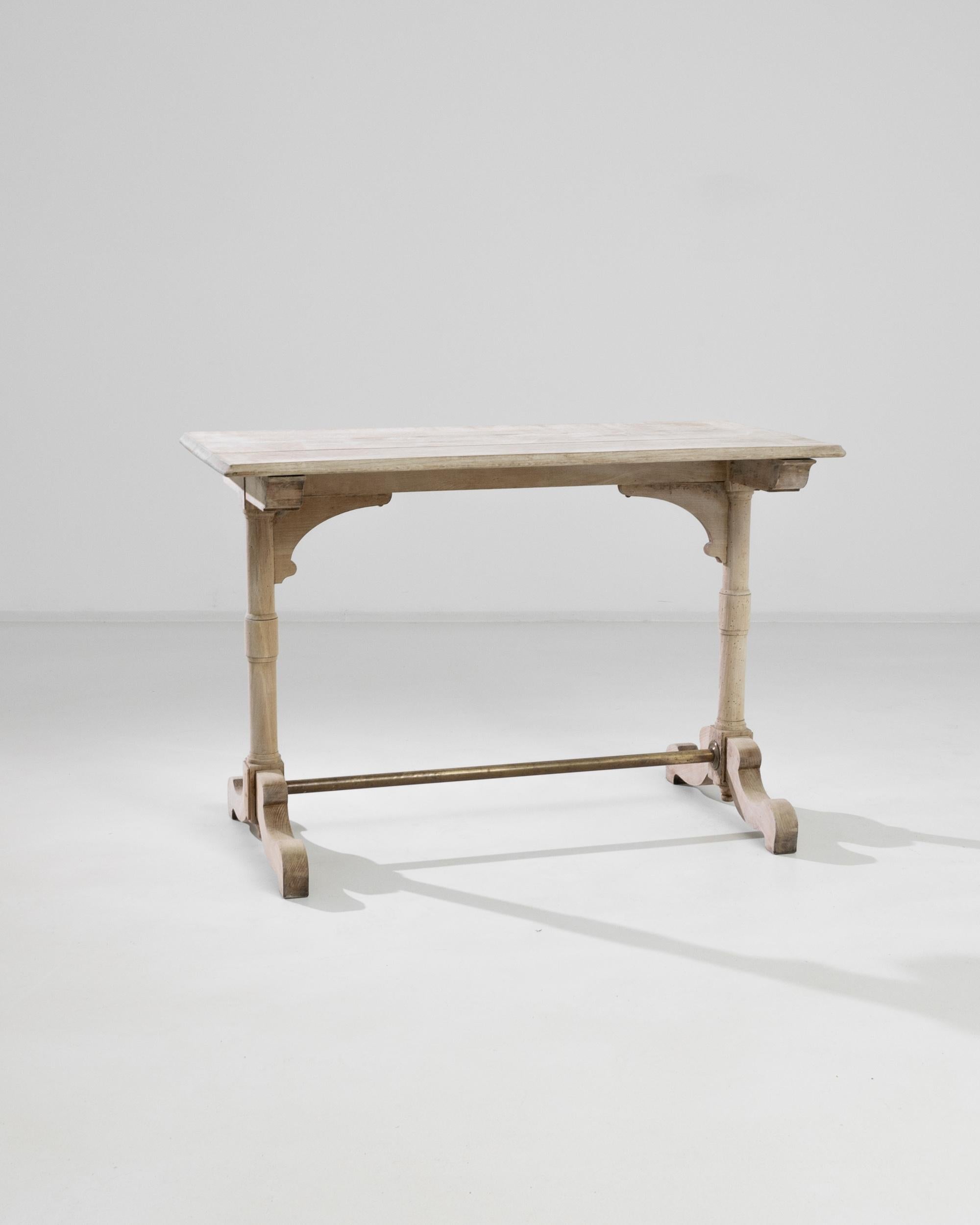 A bleached oak table produced in 1900s France. Fit with gently-aged oak and a simple brass crossbar, this table is a tastefully understated piece. Hand-turned legs, smoothly cut feet, and an artfully formed top creates a bistro table ready to serve