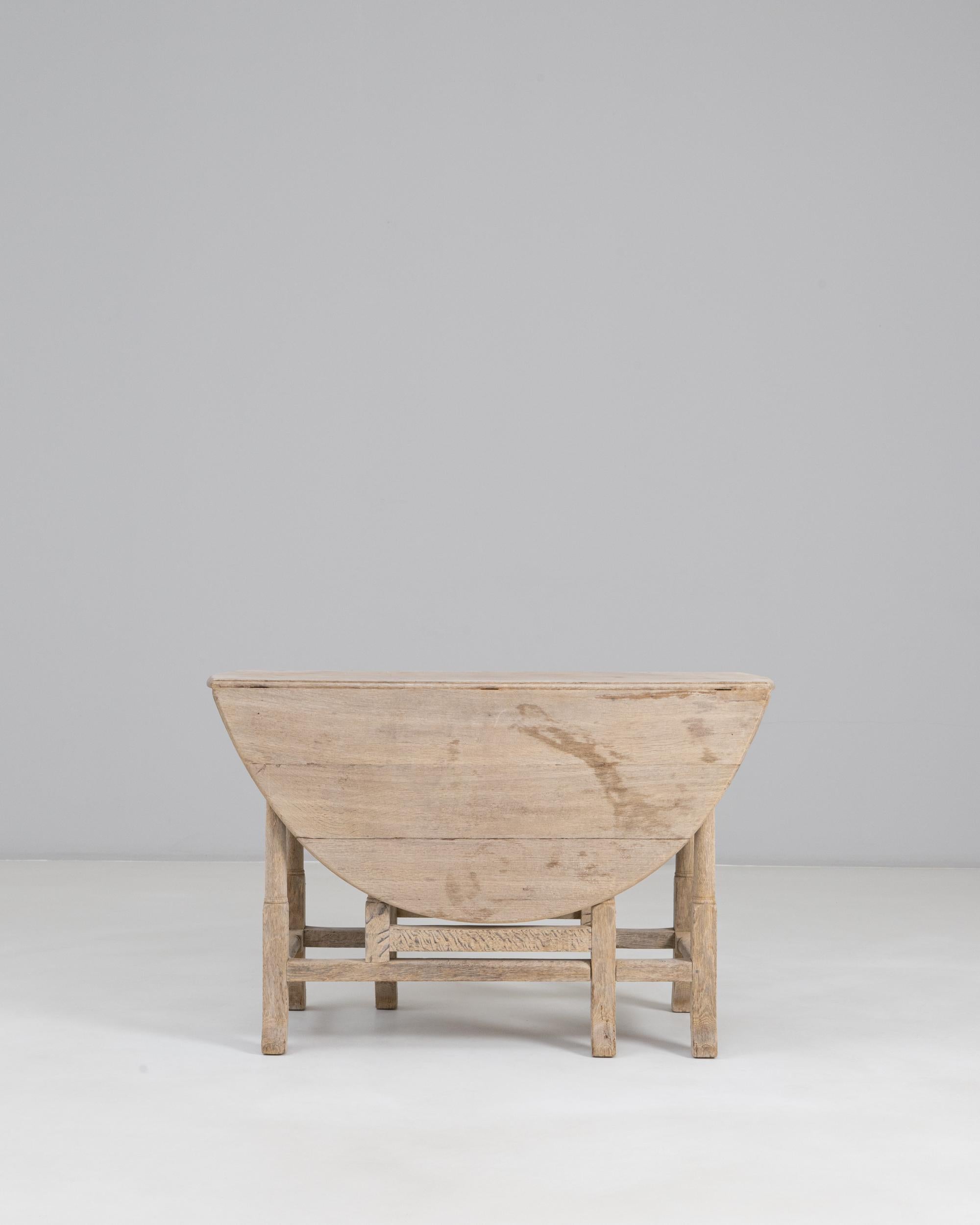 1900s French Oak Drop Leaf Table. This versatile table exemplifies early 20th-century French craftsmanship with its solid oak construction and softly weathered, natural finish. The round top features two hinged drop leaves that fold neatly when not