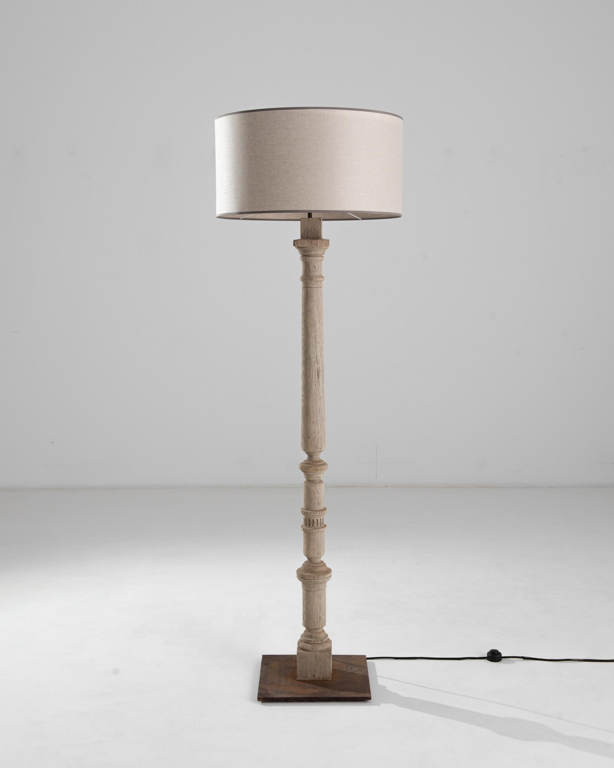 This oak floor lamp was produced in France during the turn of the century. Elevated to nearly six feet, this tall lamp exhibits a subdued palette and soft lighting. Crowned by an updated sand colored shade with a satin finish, the turned column is