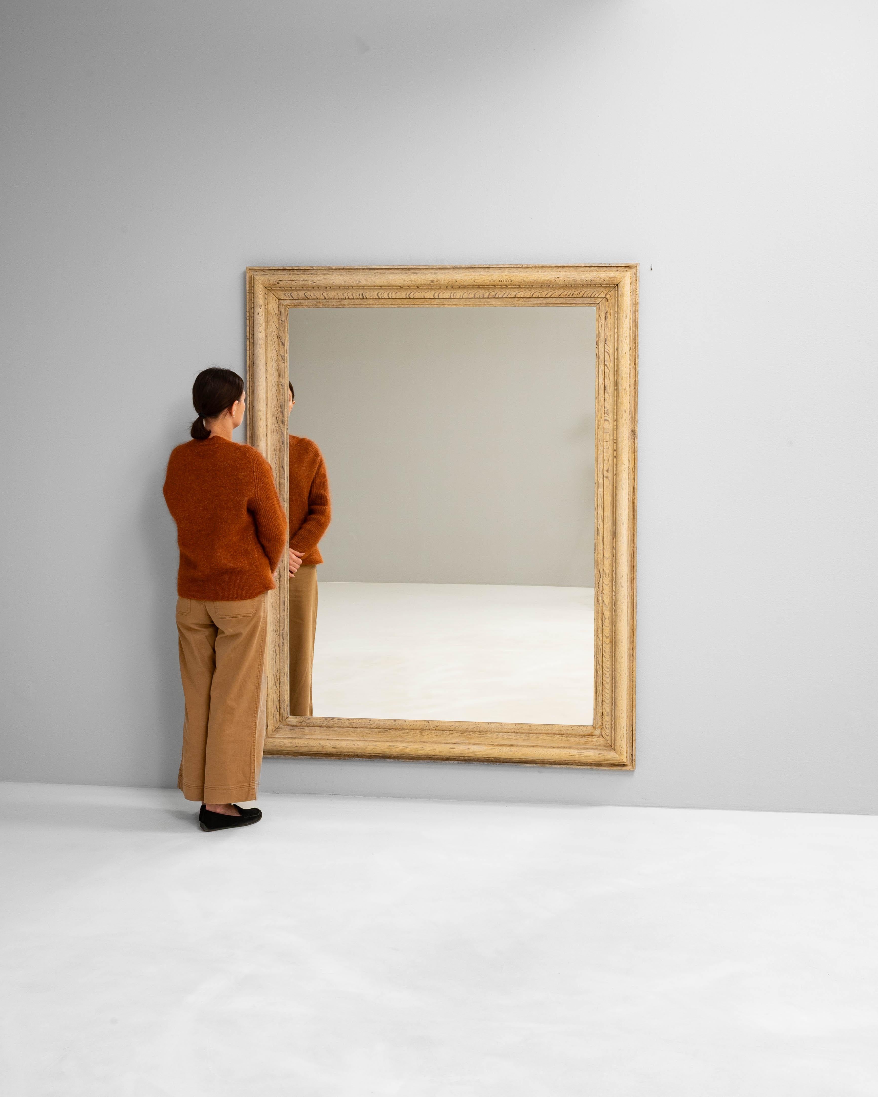 Ce miroir français des années 1900 est fabriqué en chêne massif, offrant un profil épuré et sculptural qui célèbre la beauté naturelle du grain du bois. Le cadre large présente des bords biseautés subtils et des détails sculptés le long de la