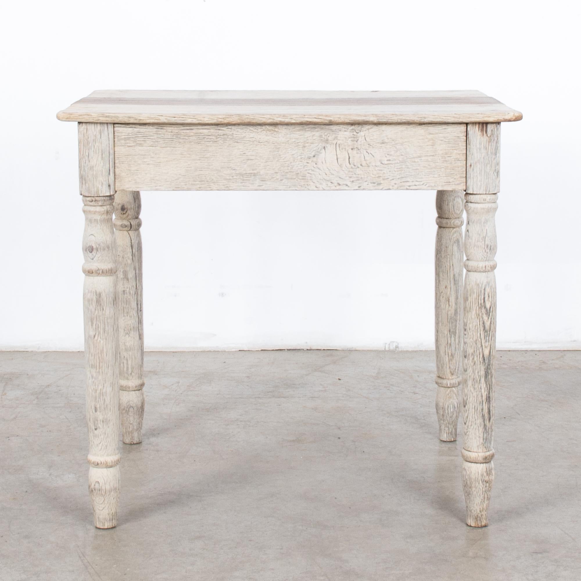 A simple oak table from turn of the century France. A square tabletop sits atop four turned legs. The pragmatic form evokes a farmhouse sensibility. The wood has been restored to a clean, bright, bleached finish, emphasizing the charming simplicity