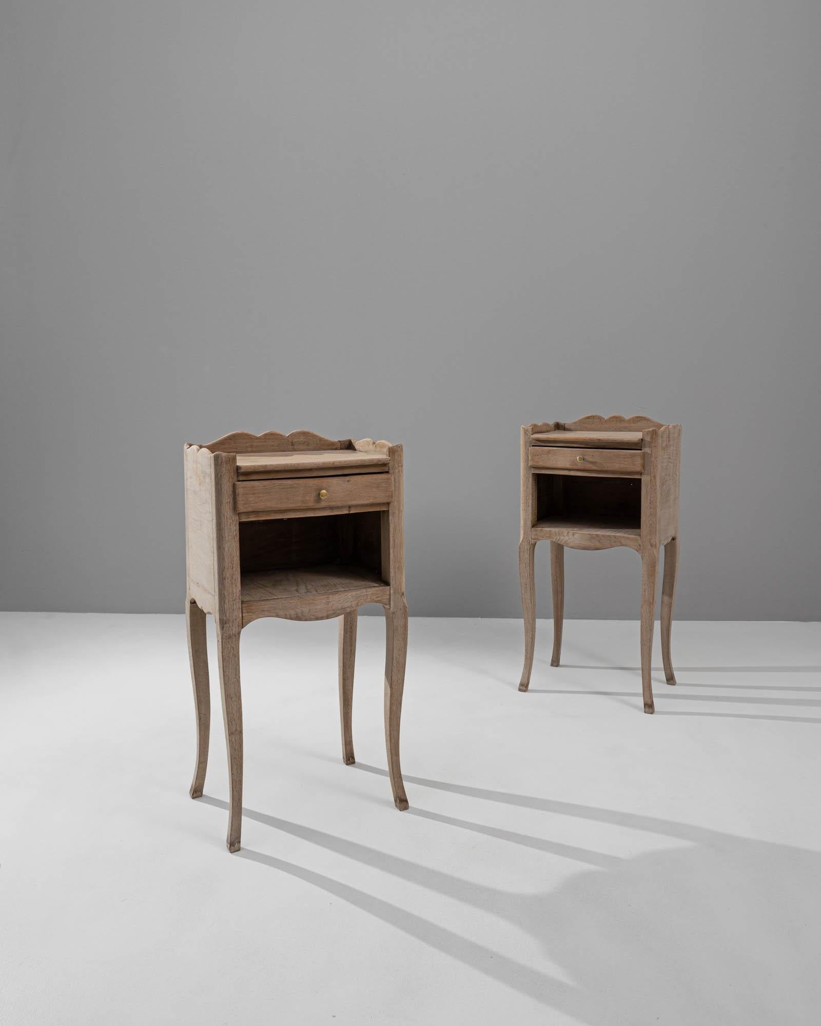 A pair of wooden side tables created in 1900s France. Petite, elegantly shaped, and brightly colored, this pair of side tables presents a neatly composed vision of craft and grace. The surface of the oak has been treated with a delicate bleaching