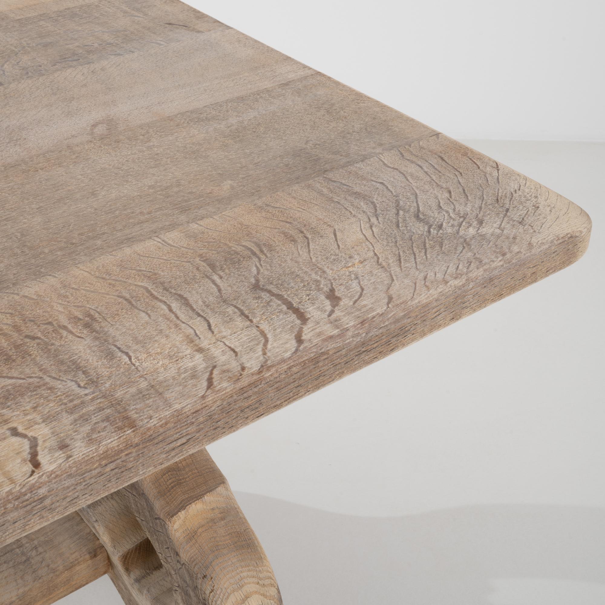A french wooden dining table made from bleached oak. This trestle table is constructed from an expansive top with playfully winding legs, undergirded by a long support beam. Exposed joinery and wooden dowel rod pegs indicate its careful