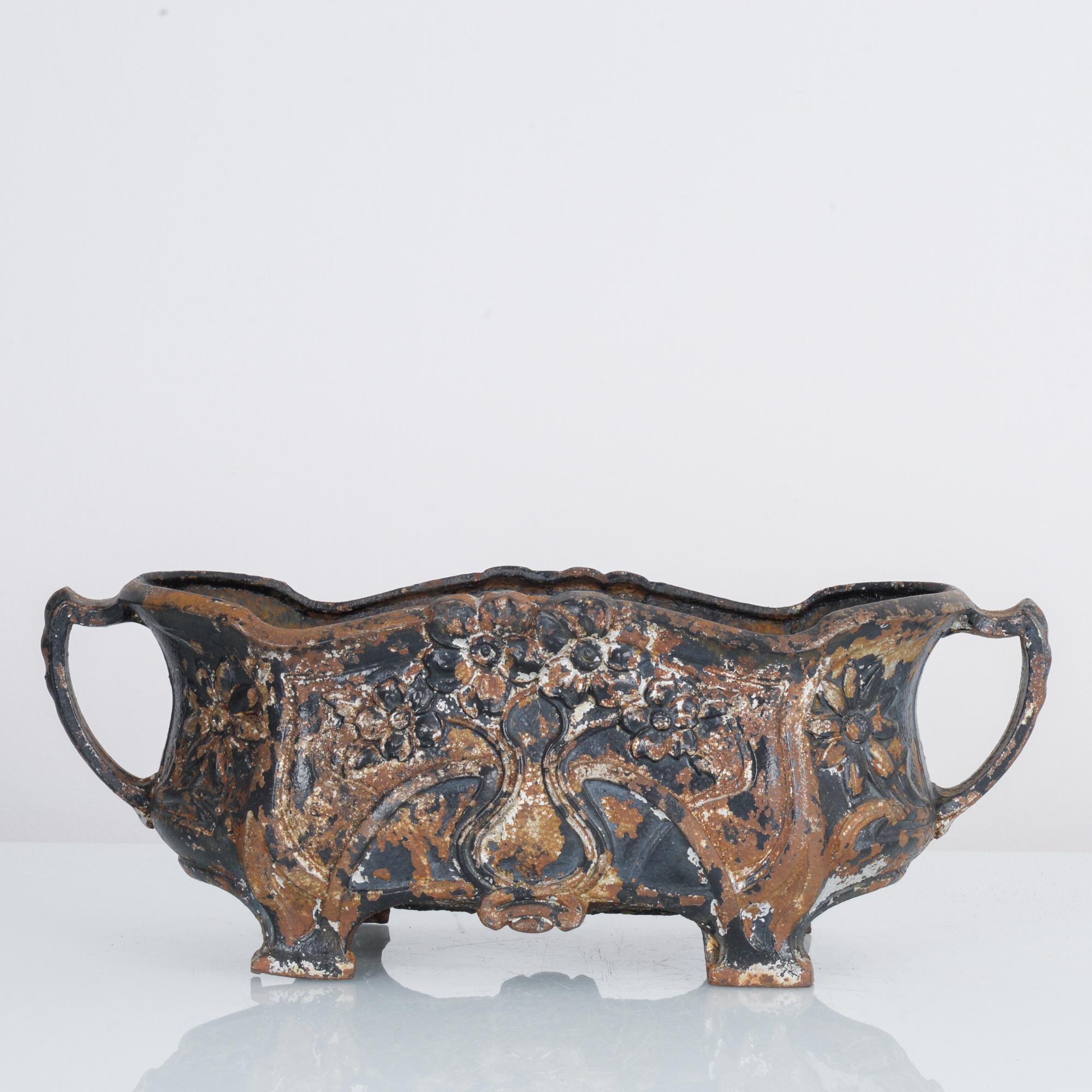 This cast iron planter was made in France, circa 1900. Originally painted black, it now displays a beautifully weathered patina. The floral designs and scalloped top give it a rustic and charming appearance. It features handles on the side and is