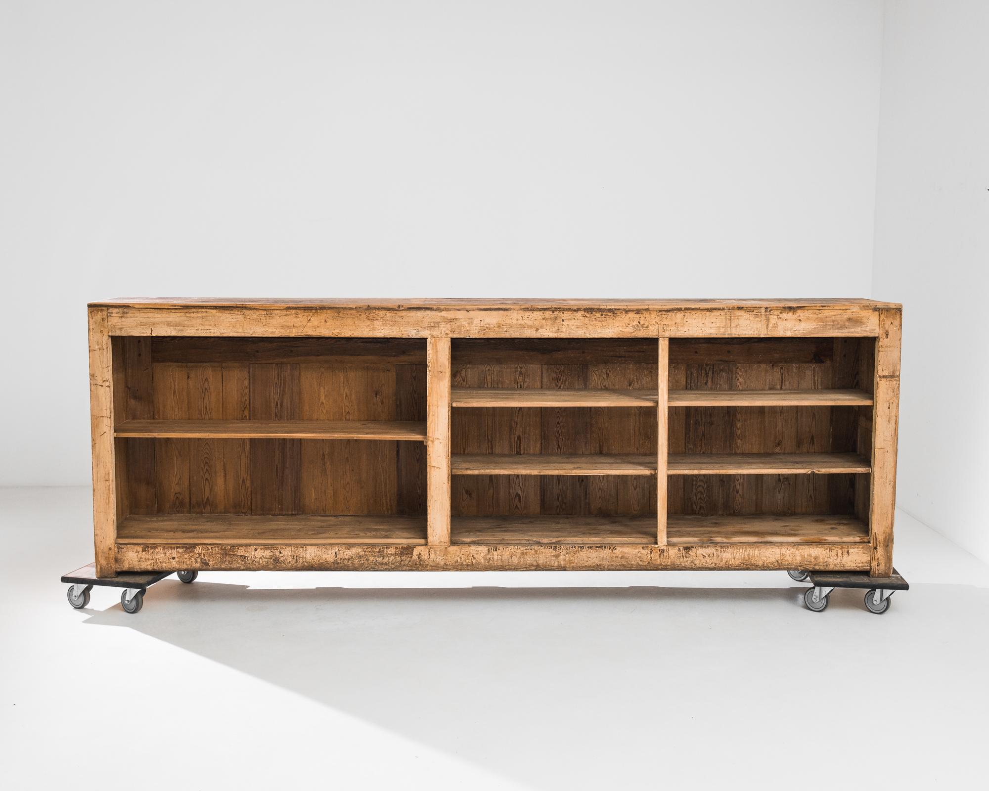 A wood patinated bar from France, produced circa 1900. A calm facade of recessed rectangular panels flanked by fluted pilasters topped by a ten foot long counter. An open back with five shelves of varying heights allows room for all materials needed
