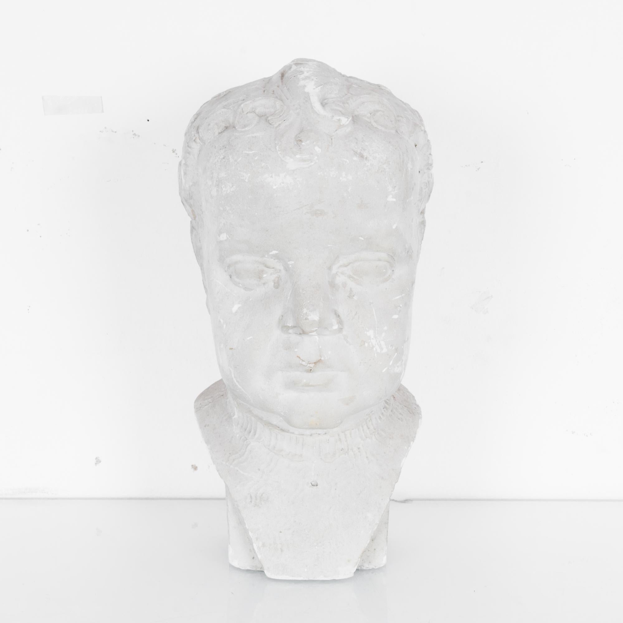 This plaster of a young child was made in France, circa 1900. The sculpture is glazed and shows the child looking straight ahead with curled hair and softly rounded cheeks. With its classical style, this work of art will certainly add elegance and a