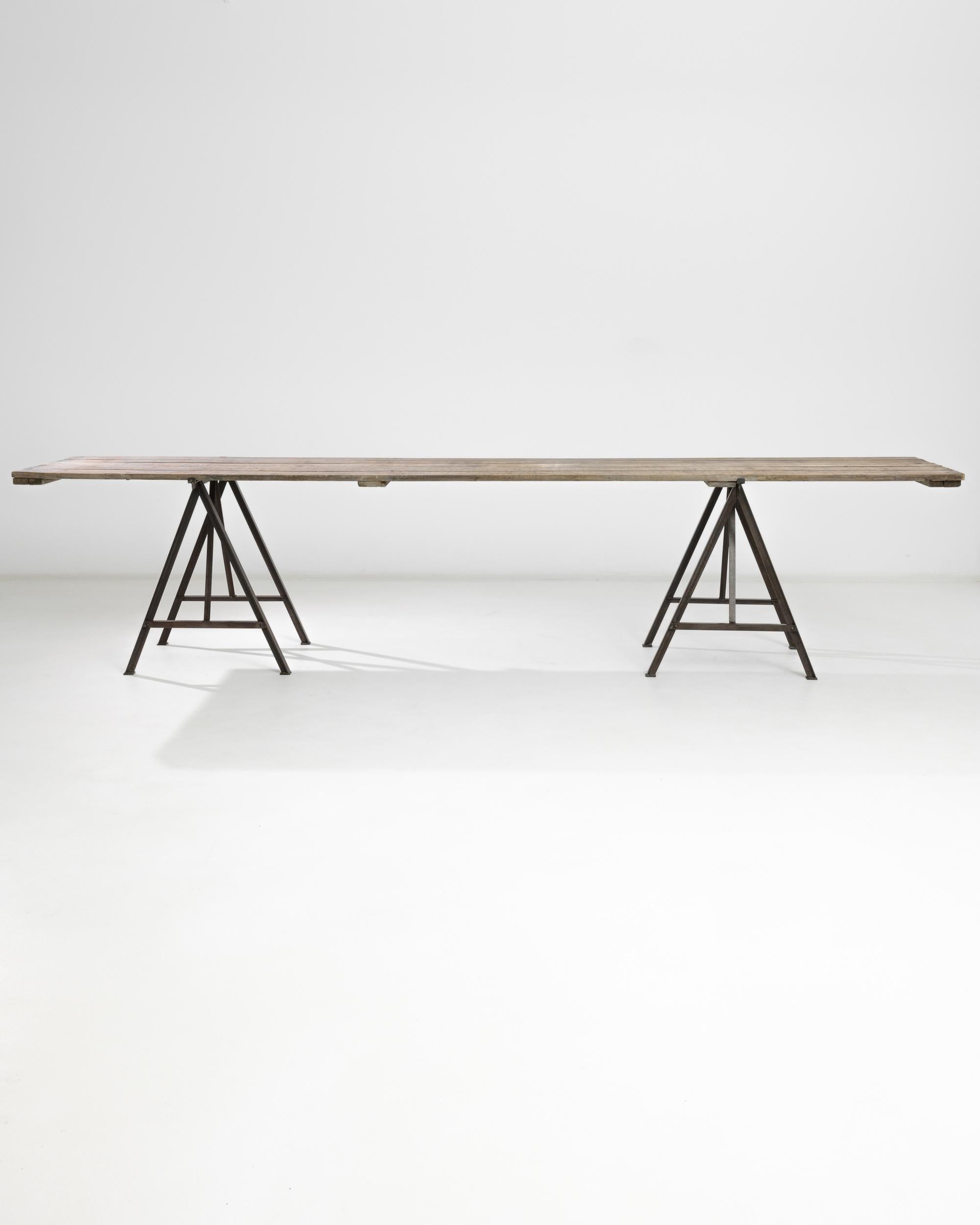 A metal table with wooden top from France, produced circa 1900. A massive vintage table, spanning an impressive length in excess of eleven feet, that manages to maintain a low-key personality even at its opulent size. A simple table constructed of