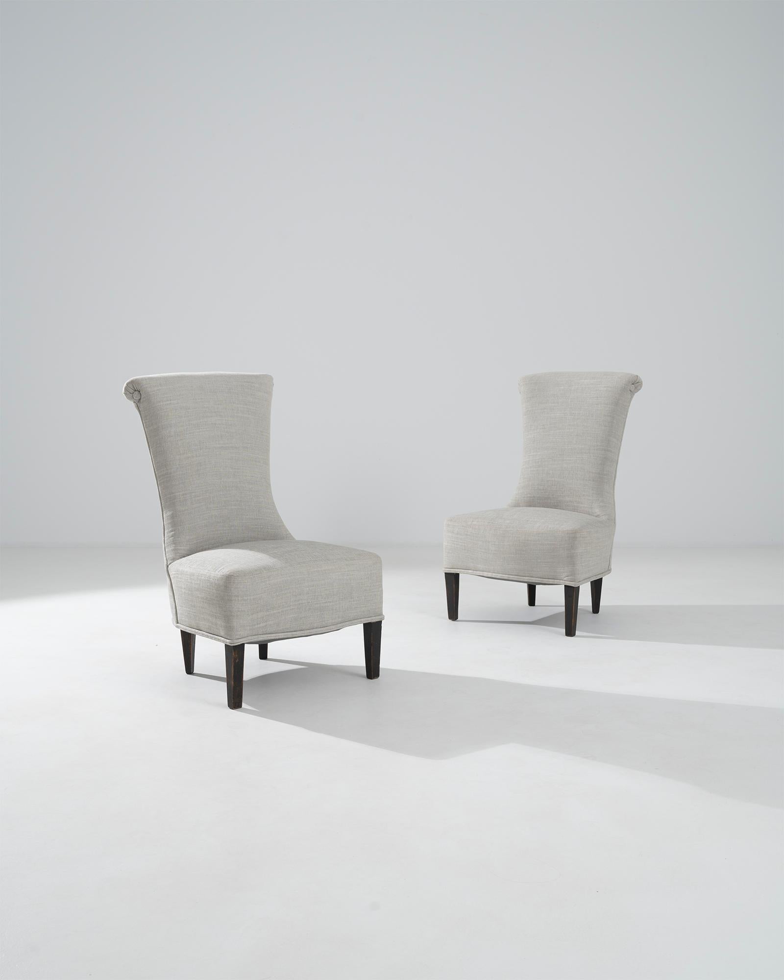 A pair of wooden upholstered chairs from 1900s France. Skinny waists and wide high-arching backs form a pleasing hourglass-like construction. A bright and clean upholstery slopes down across the back and seat of these chairs, creating a cascading