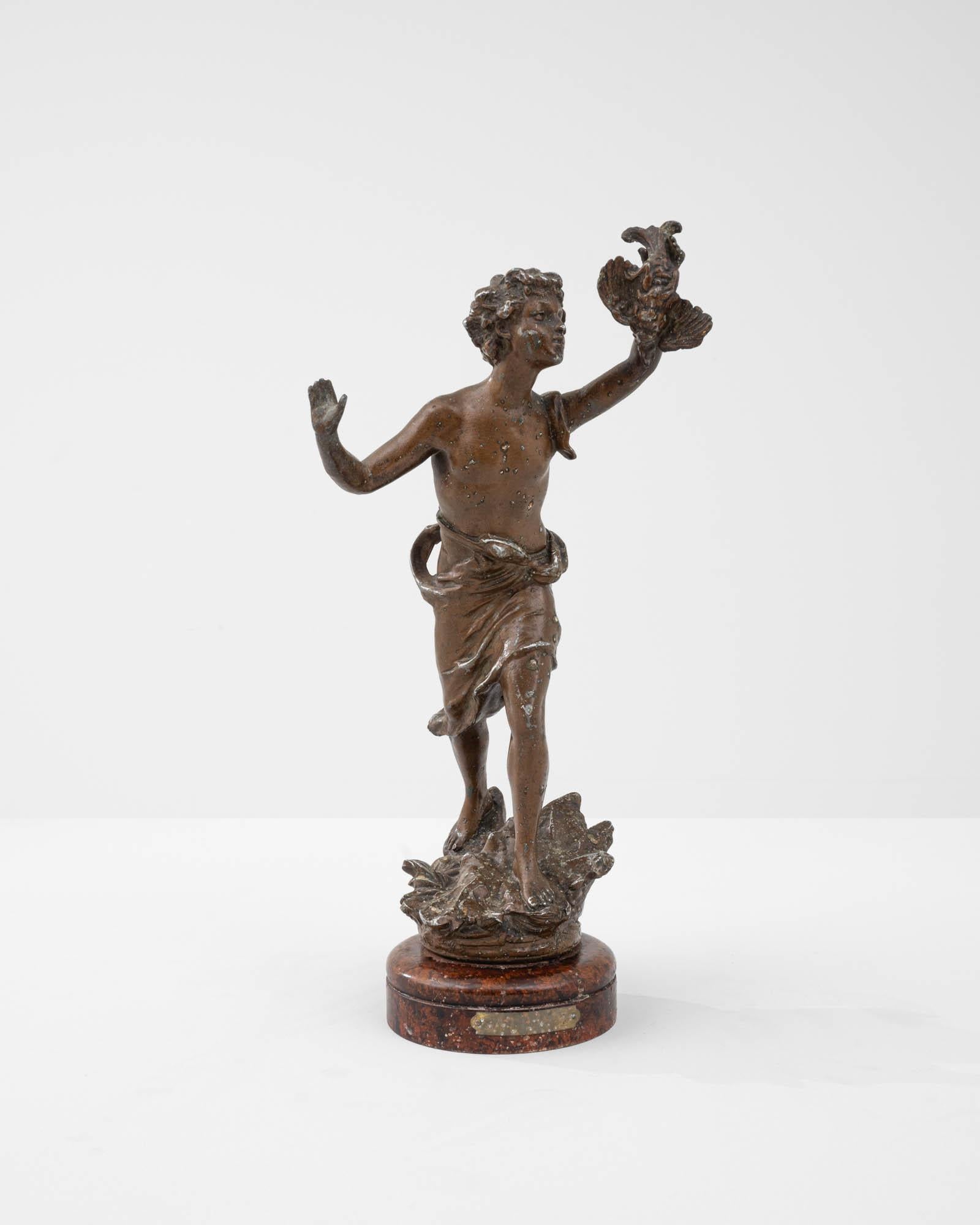 This metal figure was made in France at the turn of the 20th century. Depicting a youthful figure in motion, holding a bird aloft, the miniature sculpture recalls the classical motif of the youth and the dove. Made from tin, the metal has been