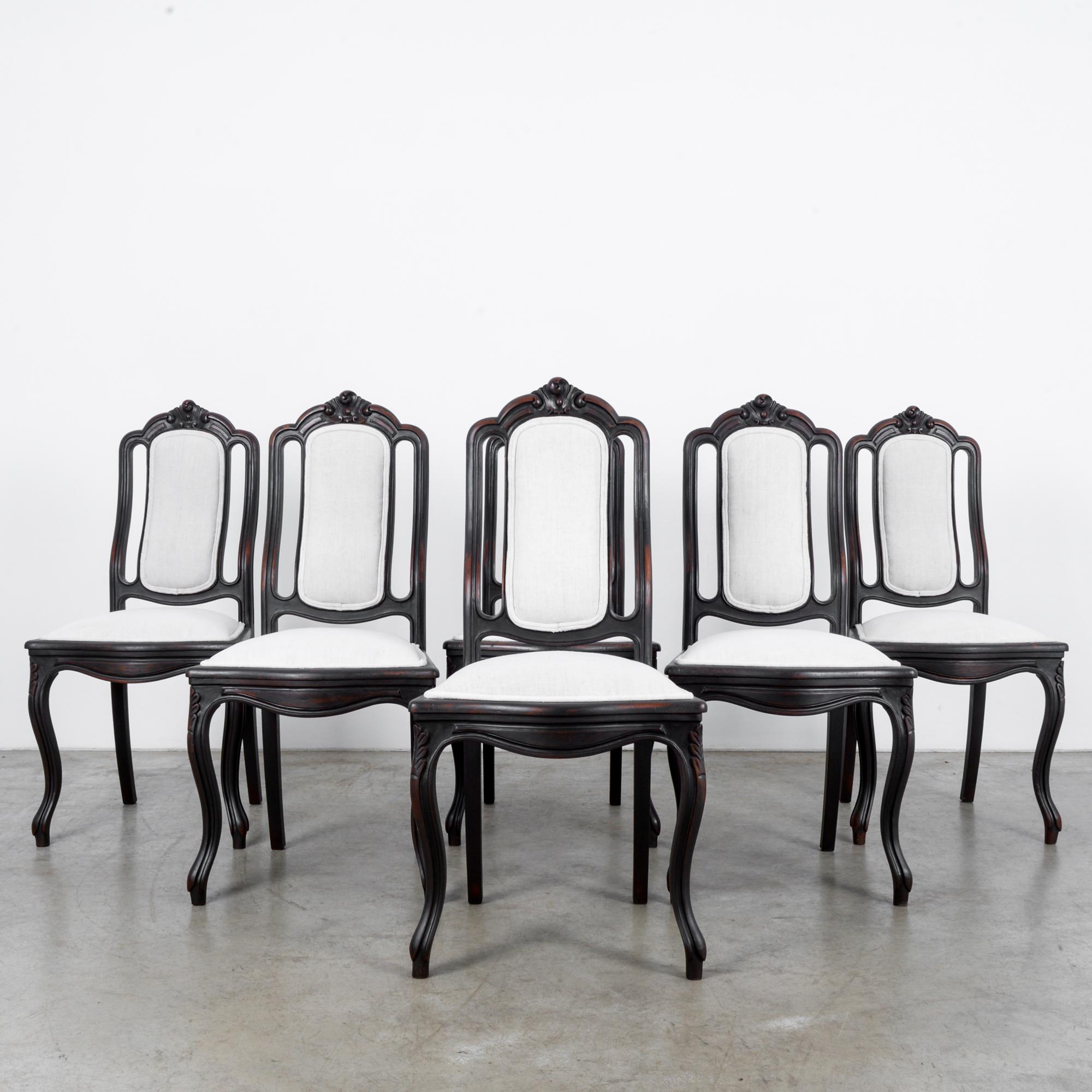 A set of six wooden upholstered dining chairs from France, circa 1900. Rich, dark wood offset by the pale gray upholstery of the seats and backs. Plush pillowing of the seats, the natural curve of the back culminating in a floral crest, and cabriole