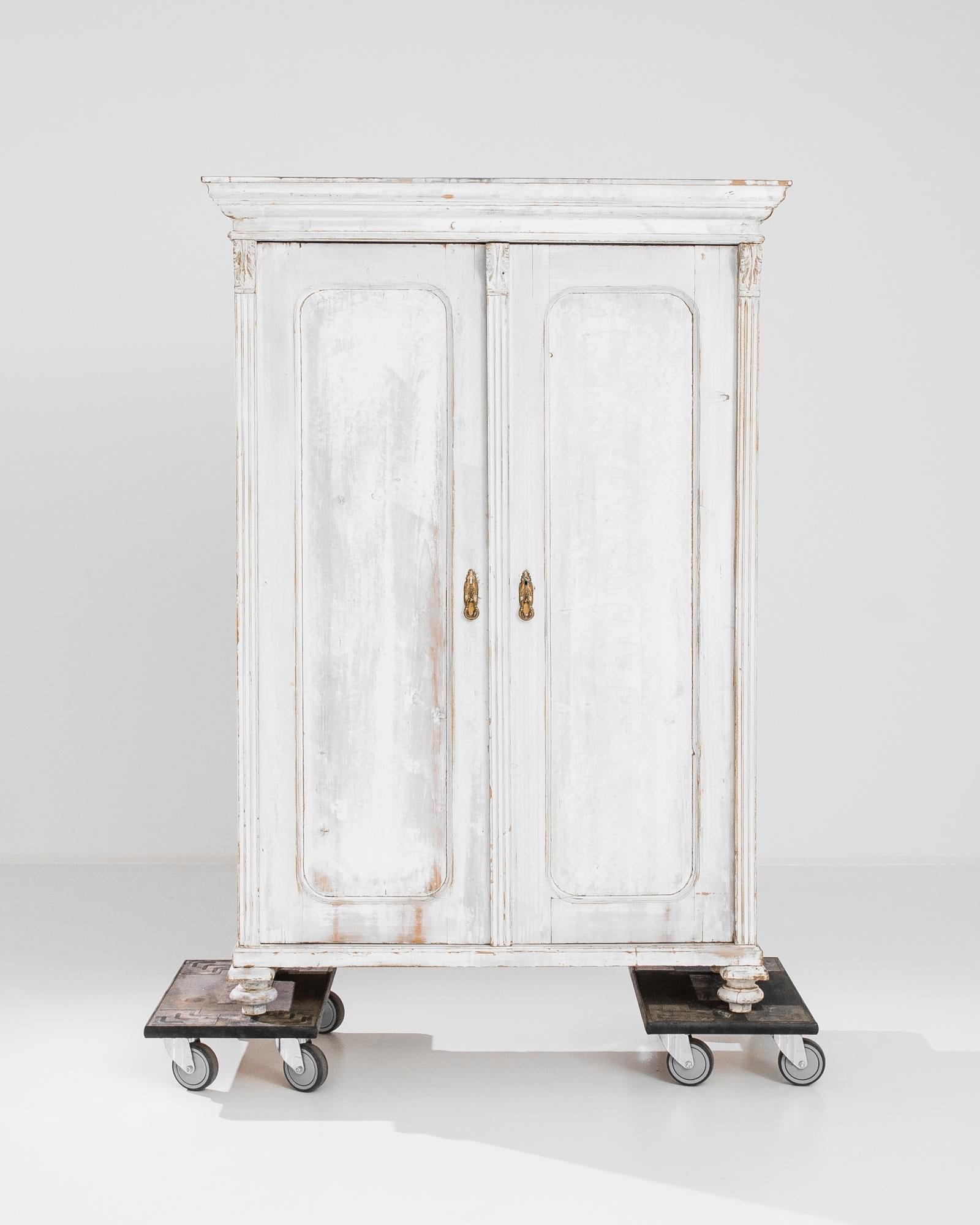 A white wooden cabinet from France, circa 1900. This handcrafted armoire stands on turned feet, guarded by a golden-brass lock. A refreshing space maker and a stylish storage. Adorned with neoclassical elements, the spacious armoire also houses an