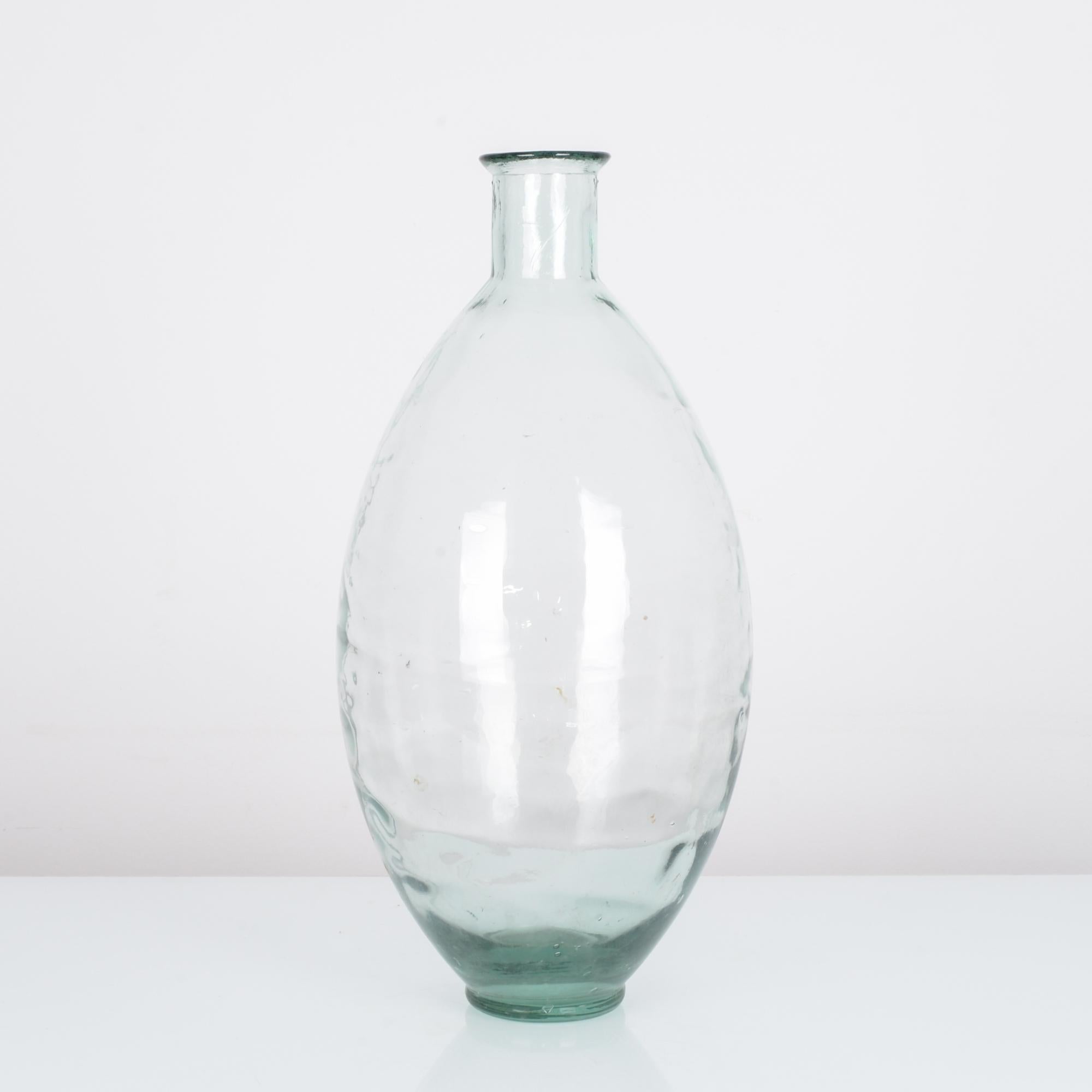 An antique 60 cm clear glass vase produced in France circa 1900. Lucid lines create an ovoid shape, evoking balance and manifesting the early cries of Modernist principles. Rippling variations across the surface catch light like bulbous prisms. A