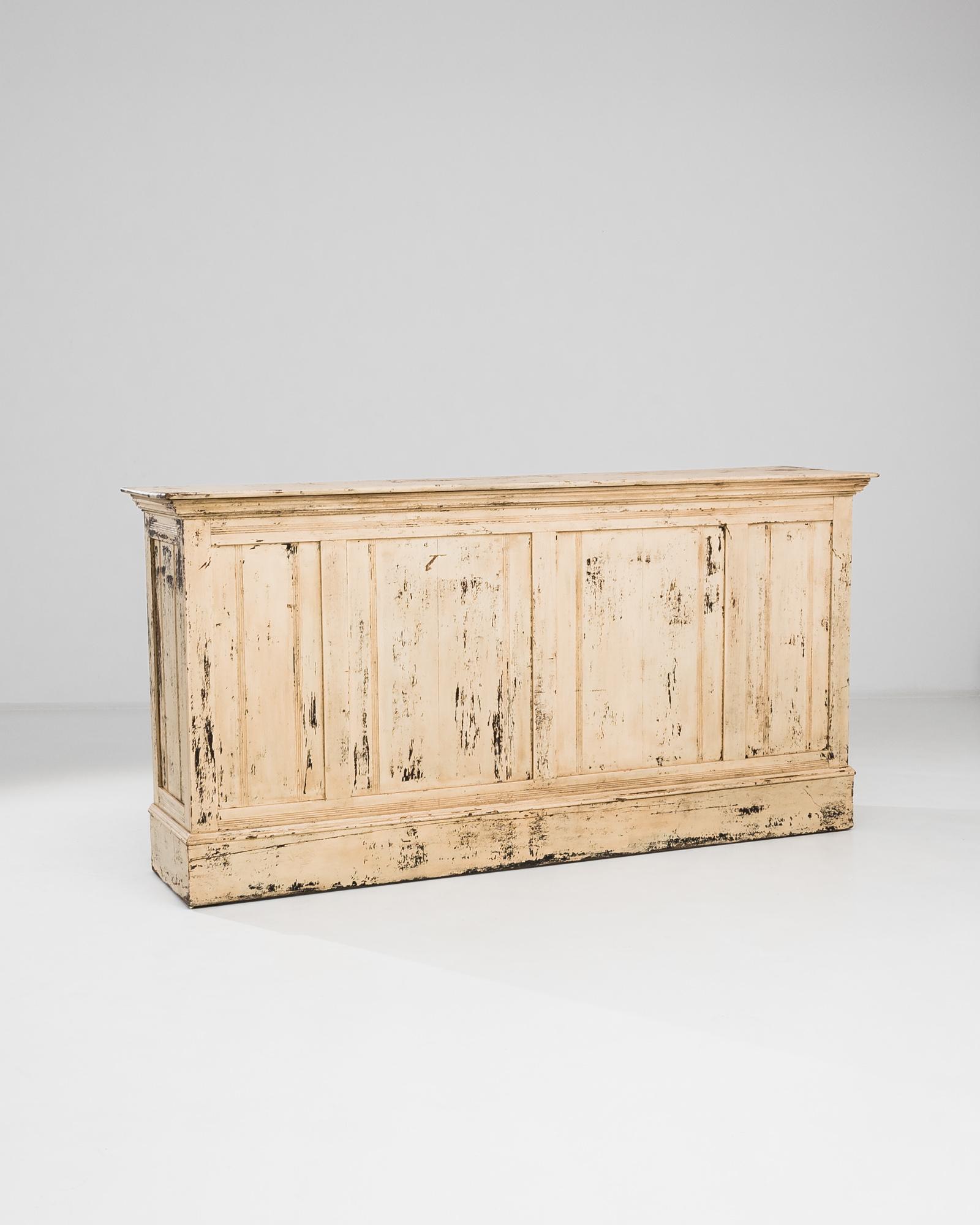 This early 1900s French wooden bar exudes antique charm with its beautifully weathered patina and timeworn finish. Crafted from solid wood, the bar features a paneled front with subtle molding details, while the back reveals open shelving for