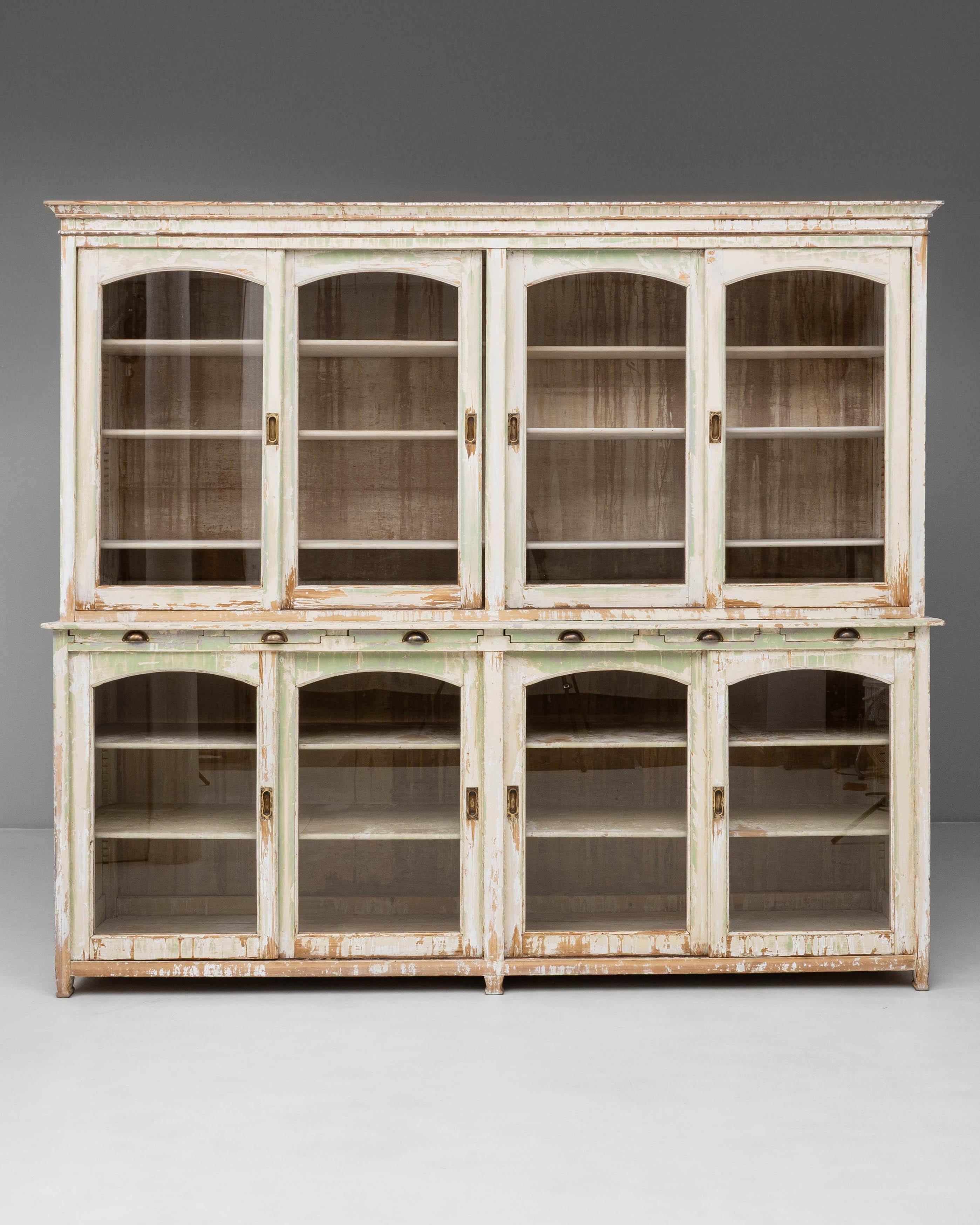 Cette vitrine en bois français des années 1900 présente une charmante finition patinée usée, soulignant sa longue histoire et son caractère. Conçue avec huit portes vitrées, quatre en haut et quatre en bas, elle offre un vaste espace de rangement