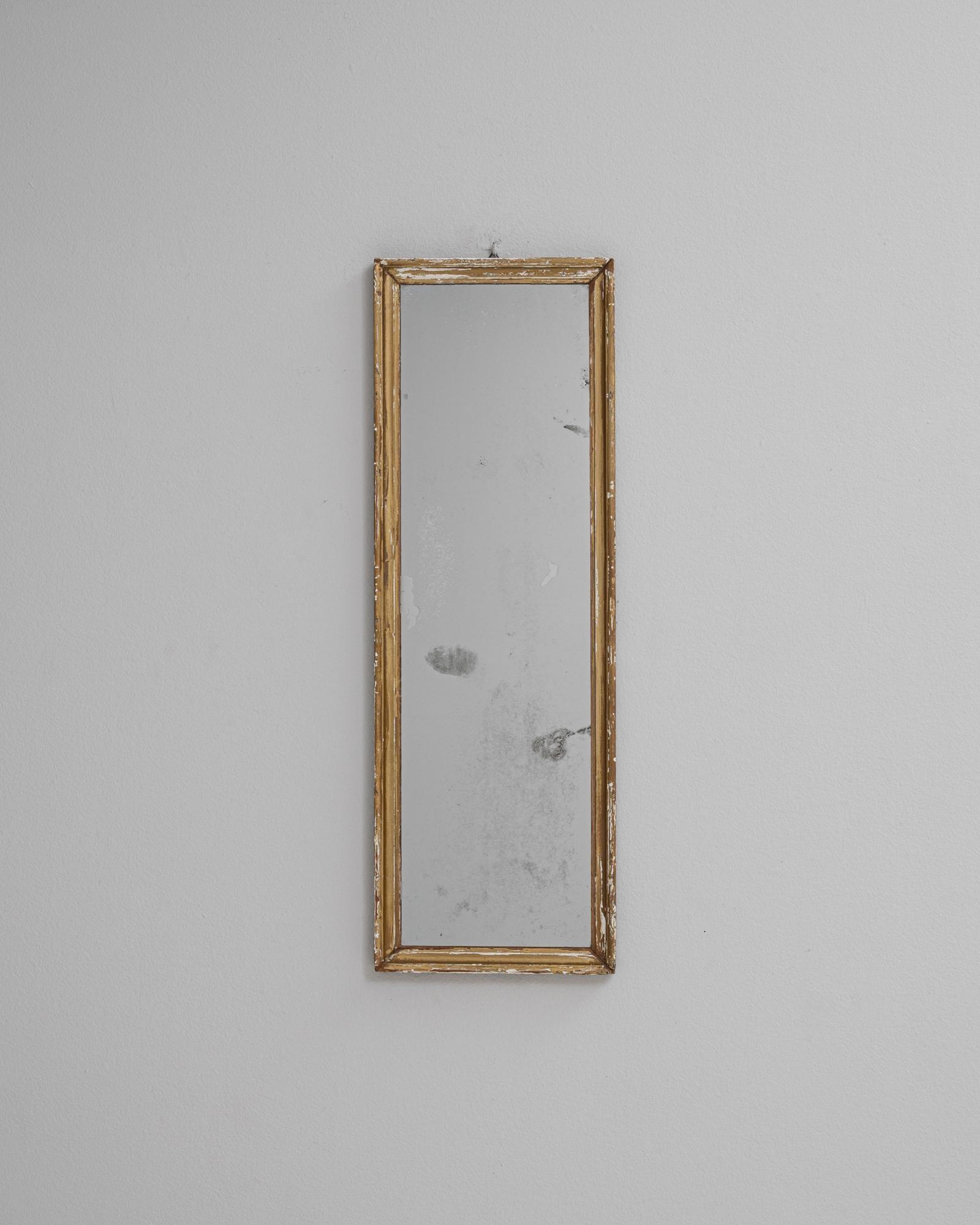 Questo specchio francese in legno patinato del 1900 presenta un profilo alto ed elegantemente stretto incorniciato in legno dorato con dettagli naturalmente usurati che ne evidenziano l'età e l'autenticità. La doratura attenuata e le sottili