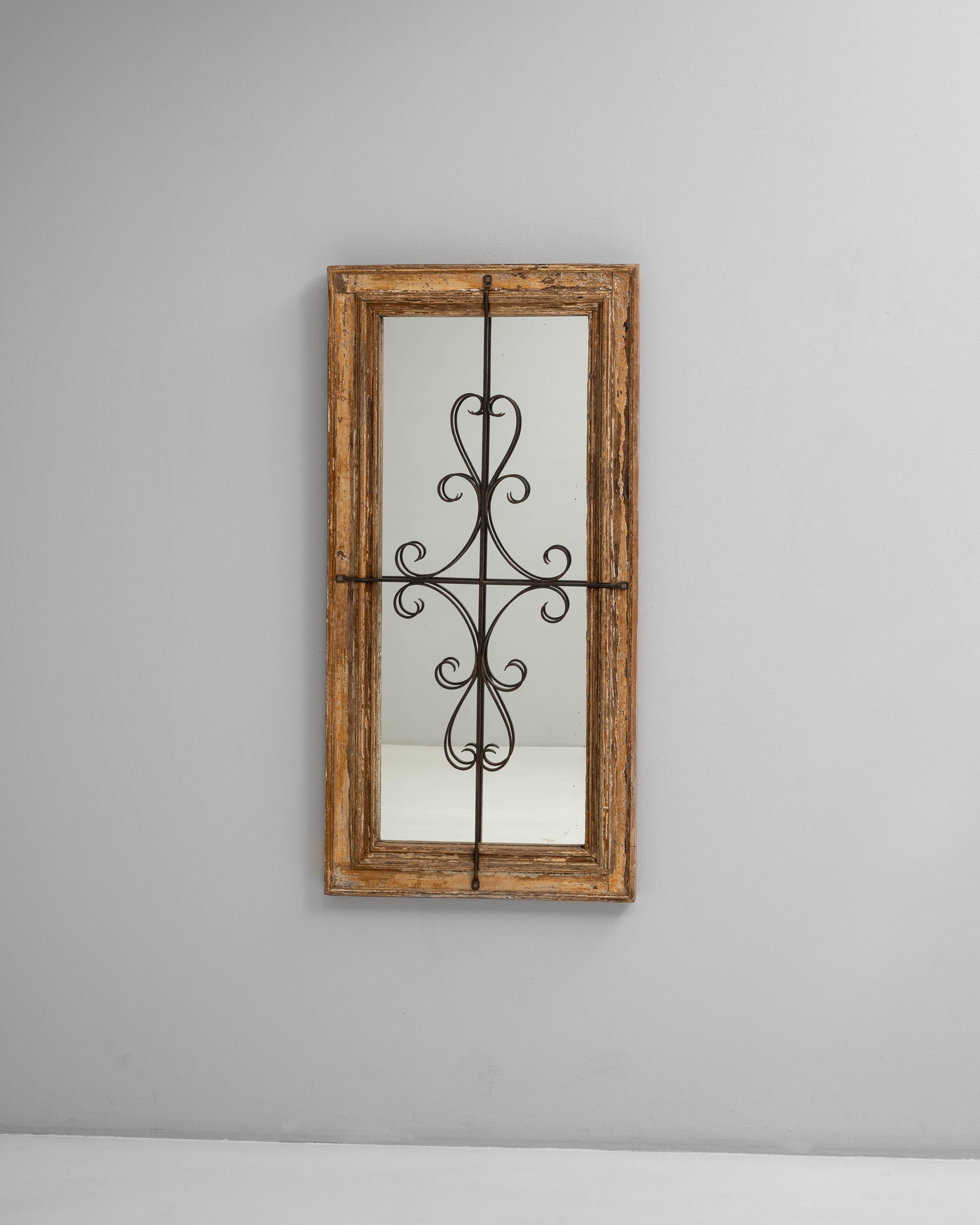 Miroir français des années 1900 en bois patiné qui se distingue par une combinaison frappante de texture rustique et d'ornementation en fer forgé. Le cadre conserve sa surface originale, usée par le temps, avec des couches de patine adoucie qui