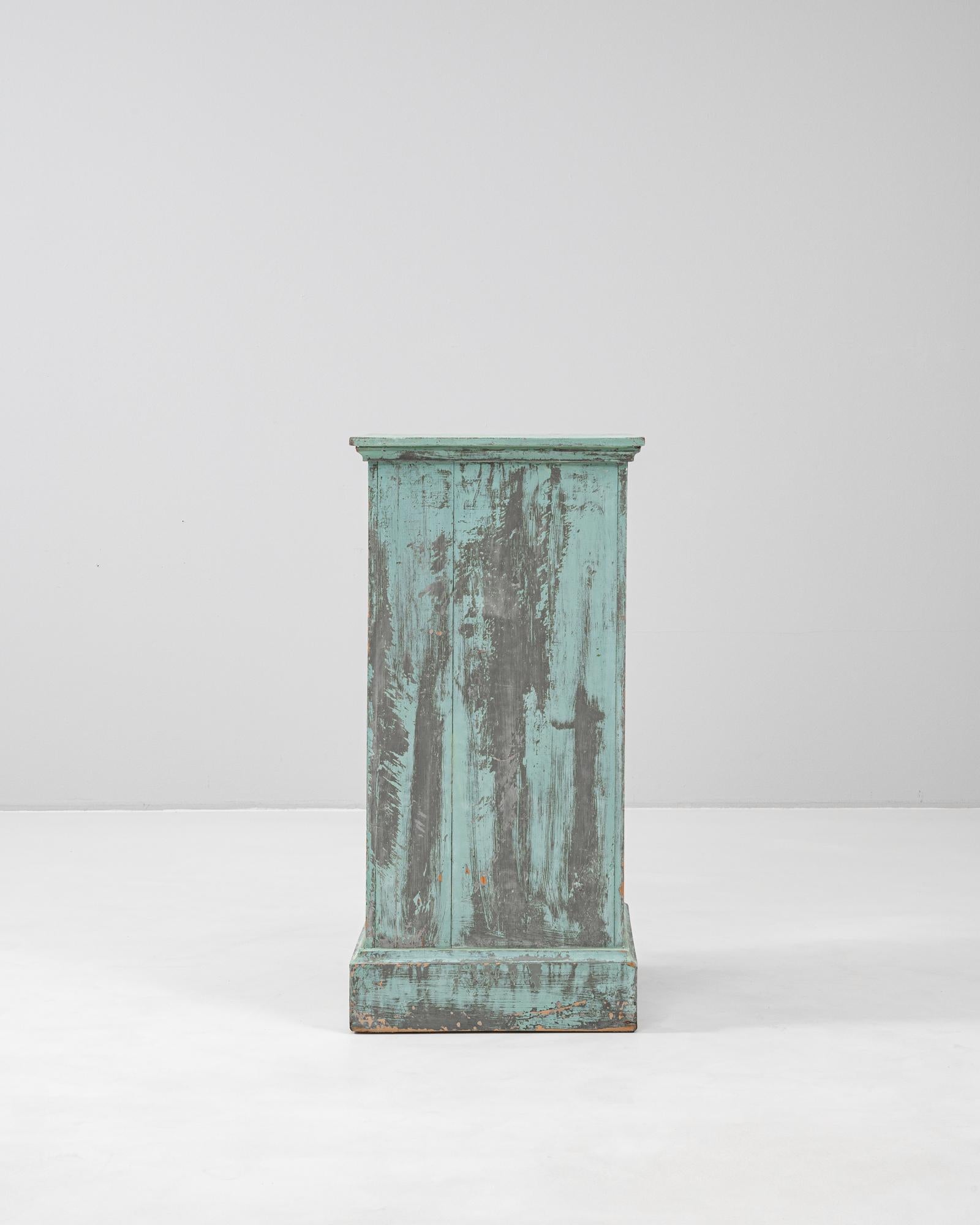 This 1900s French wood pedestal features a beautifully weathered patinated finish in shades of turquoise and charcoal, revealing traces of its original paint and age-worn surface. The rectangular form is elevated by a molded top and plinth base,