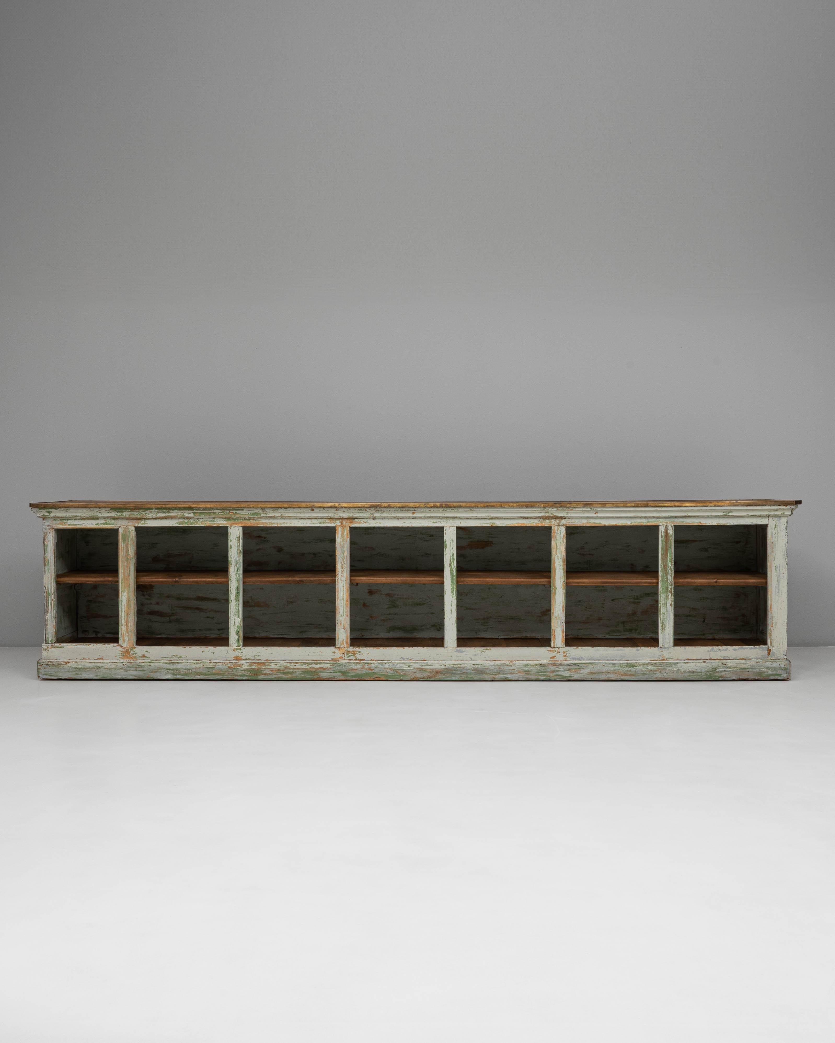 This 1900s French Wood Patinated Shop Counter with Open Storage exemplifies the character and craftsmanship of early 20th-century French mercantile furniture. Constructed from solid wood, it features a beautifully distressed painted finish in soft