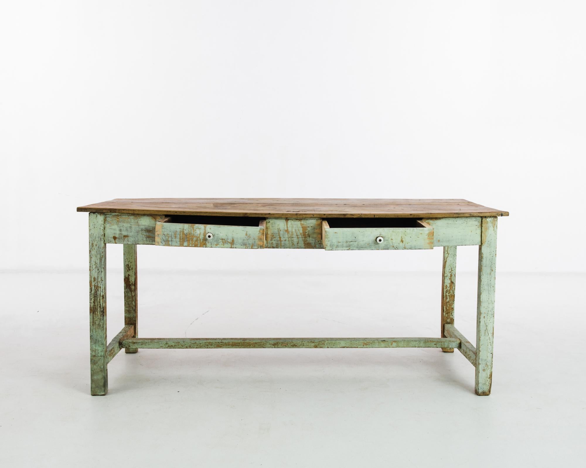 Embrace the vintage allure of this 1900s French wood patinated table, a testament to timeless craftsmanship and character. This solid wood workshop table boasts an original green painted leg finish, adding a touch of rustic charm. The natural top
