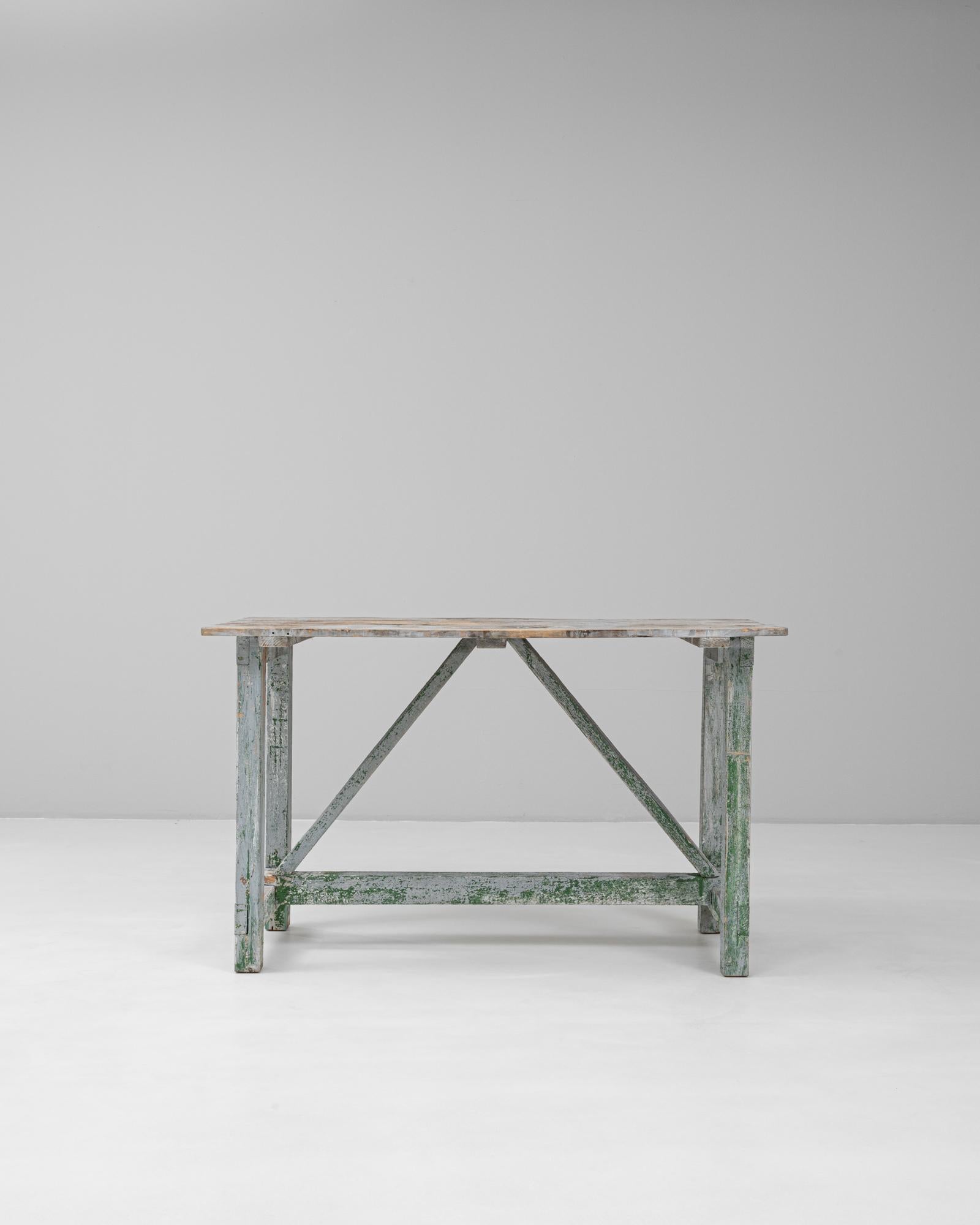 Esta mesa de madera francesa de 1900 muestra el encanto intemporal de la antigüedad y la artesanía, con una pátina bellamente desgastada en suaves capas de tonos verdes y grises. La parte superior rectangular descansa sobre una robusta base de