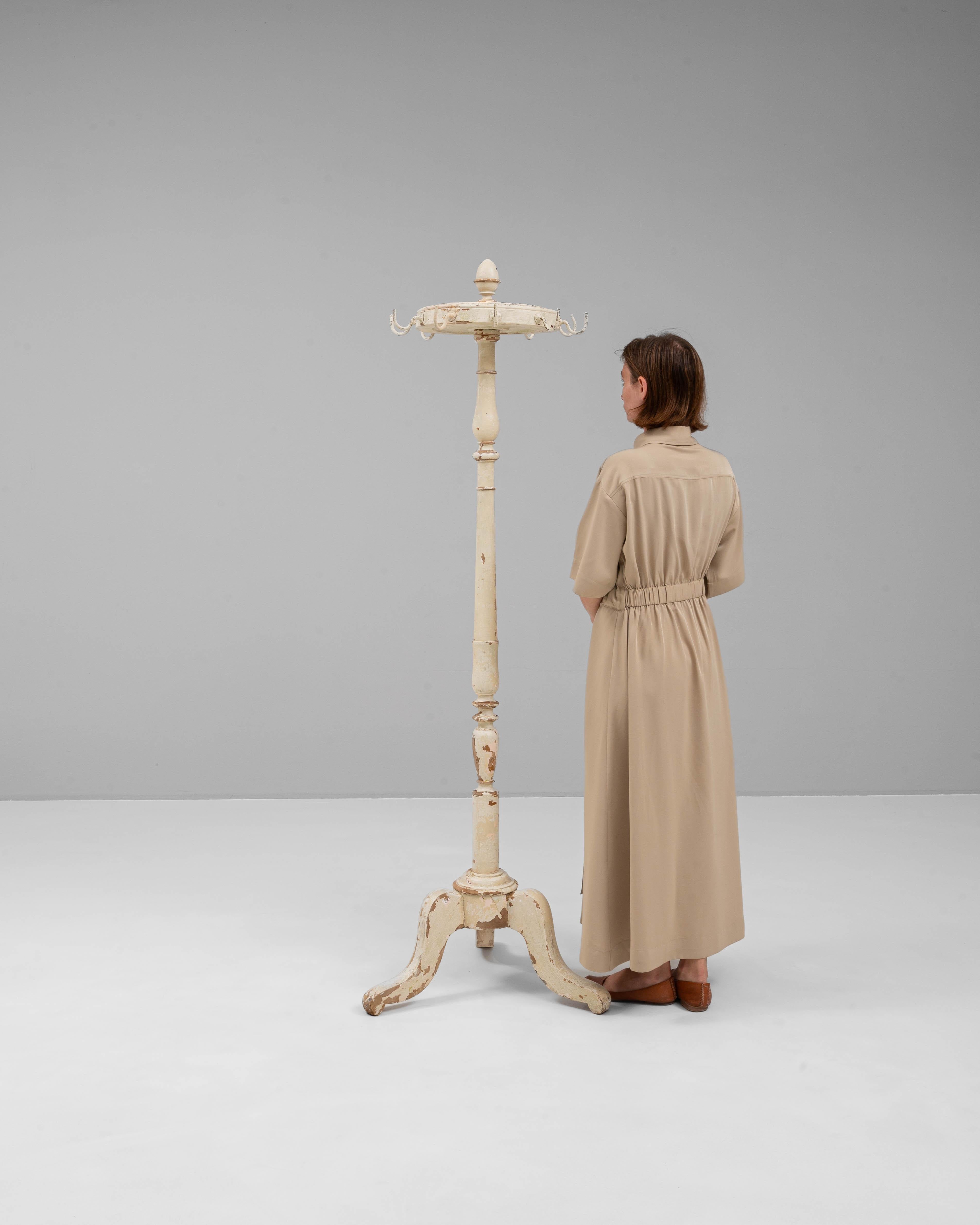 Dieser französische Fußbodenaufhänger aus der Zeit um 1900 verbindet Funktionalität mit rustikalem Charme. Er ist aus Holz gefertigt und verfügt über eine anmutig gedrechselte Mittelsäule und einen dreibeinigen Fuß, der für Stabilität sorgt. Die