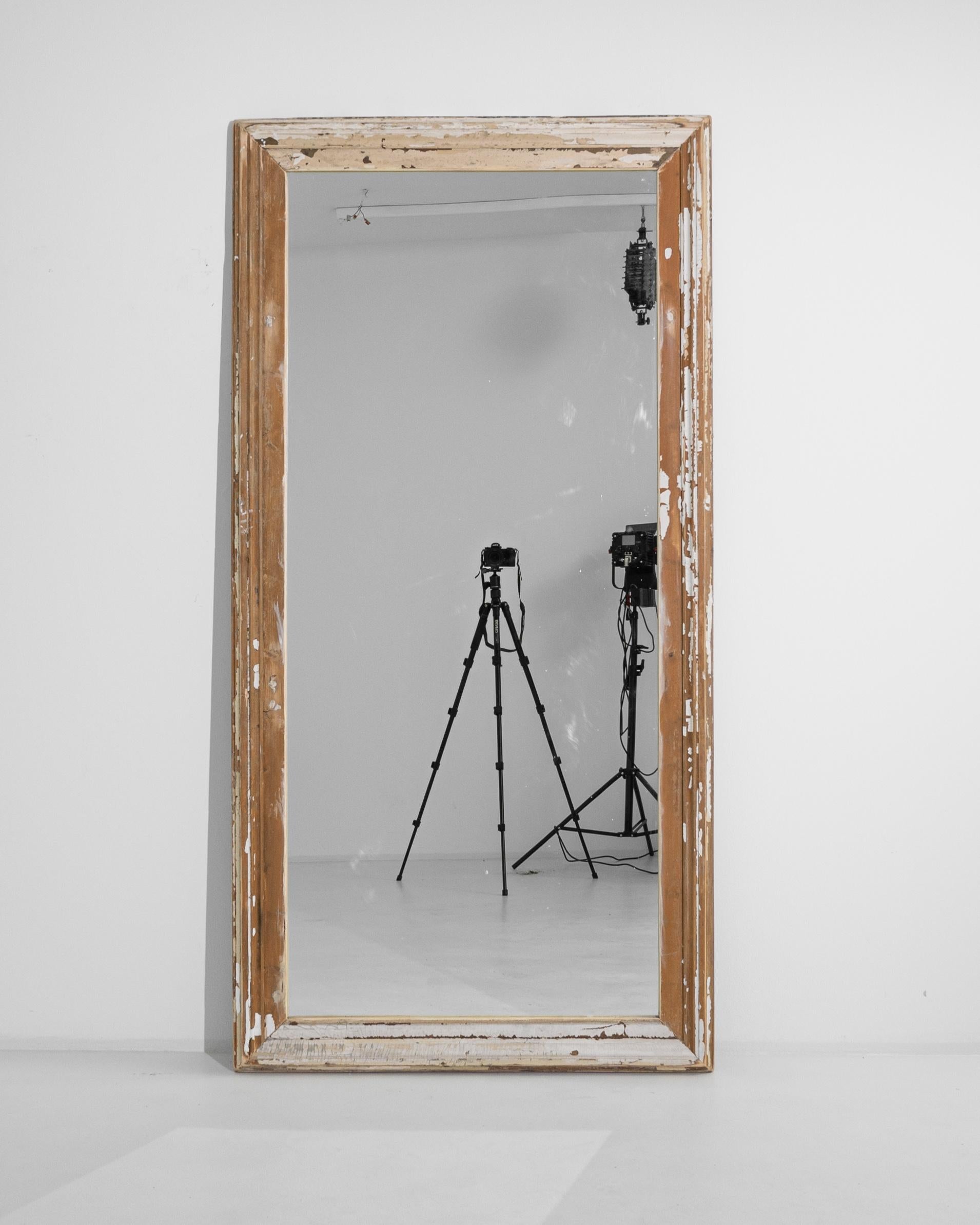 This 1900s French Wood Mirror exudes a shabby chic appeal that brings with it a sense of rustic elegance. The frame's white patina, bearing the gentle caress of time, tells its own story through each chip and scratch. Crafted in a period known for
