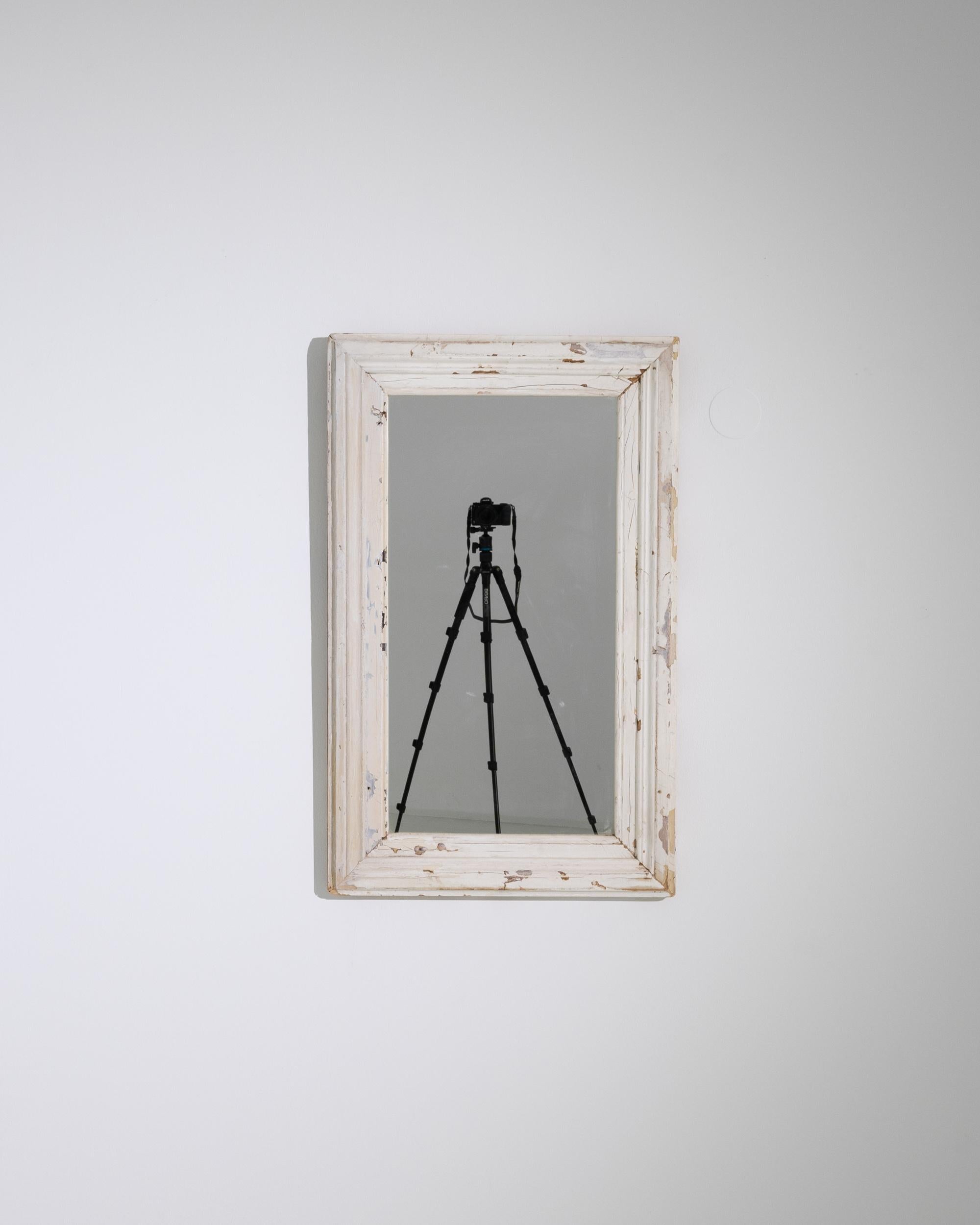 This 1900s French Wood White Patinated Mirror embodies the quintessential shabby chic aesthetic, offering a blend of rustic charm and understated elegance. The frame, adorned with layers of chipped white paint, reveals the passage of time, adding